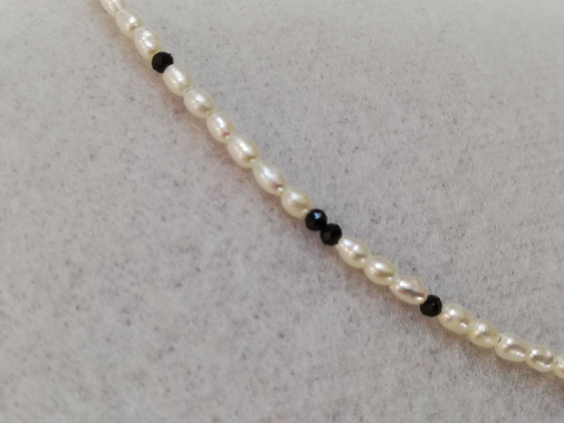 weiße Süßwasserzuchtperlenkette in Reiskorngröße mit kleinem facettiertem Spinell