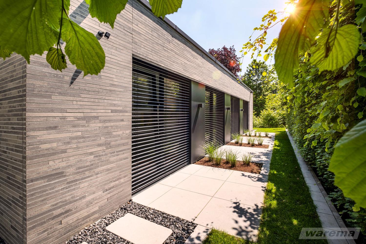 Außenjalousien für Sichtschutz und Sicherheit für Ihr Zuhause bei LS Sonnenschutz in Groß-Umstadt kaufen. Wir beraten Sie gerne zu verschiedenen Modellen und Farben im Raum Darmstadt, Dieburg, Frankfurt, Aschaffenburg, Odenwald. Heruntergelassene Außenjalousie an Fassade bei Sonnenschein, geöffnete Lamellen, Link zu Produktseite Jalousien & Raffstore