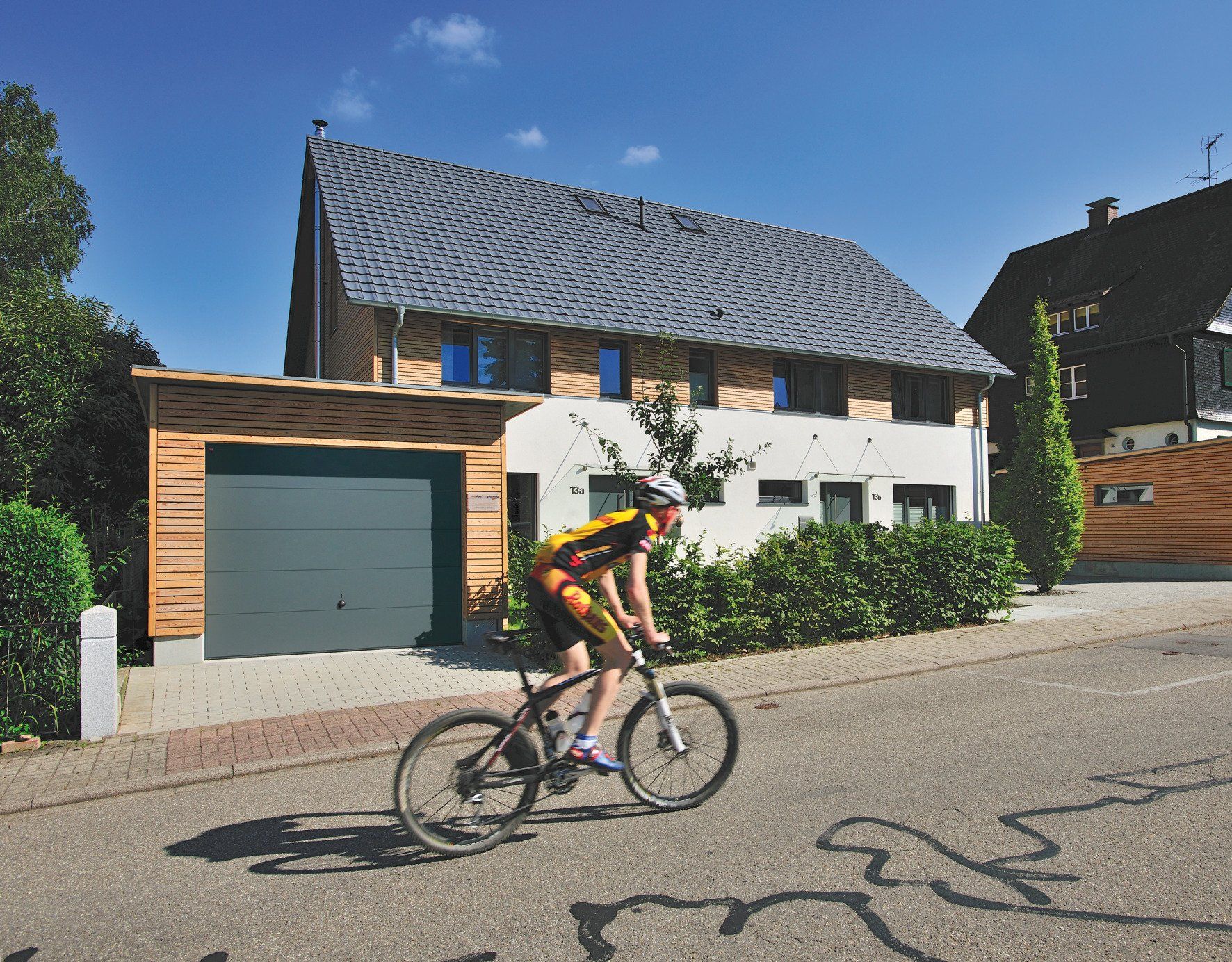Fahrradfahrer fährt an Haus mit Garage vorbei, modernes Sektional-Garagentor in anthrazit