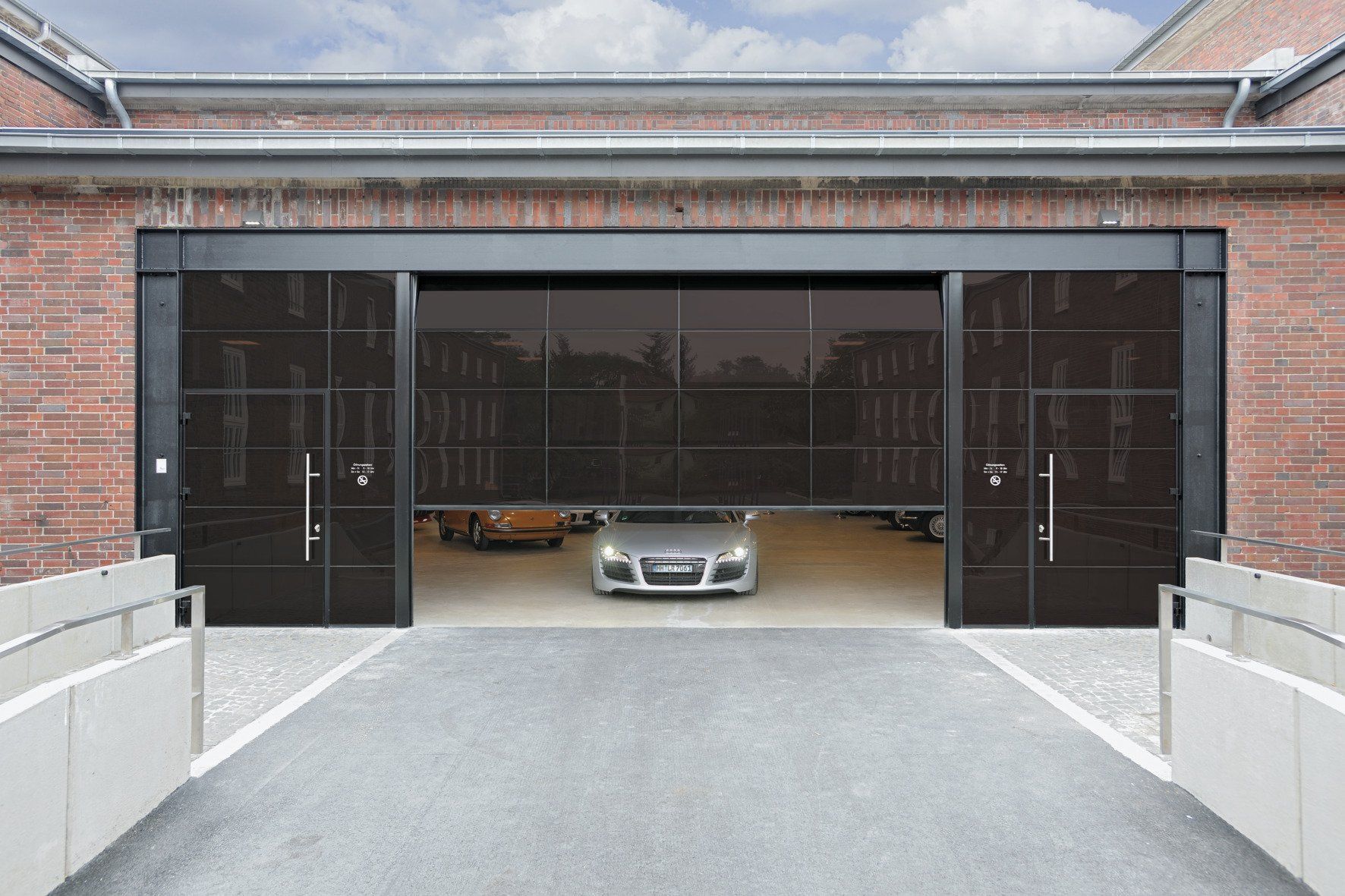 Silbernes Auto fährt aus großer Garage mit dunklem, nicht durchsichtigem Glas und Schiebetüren