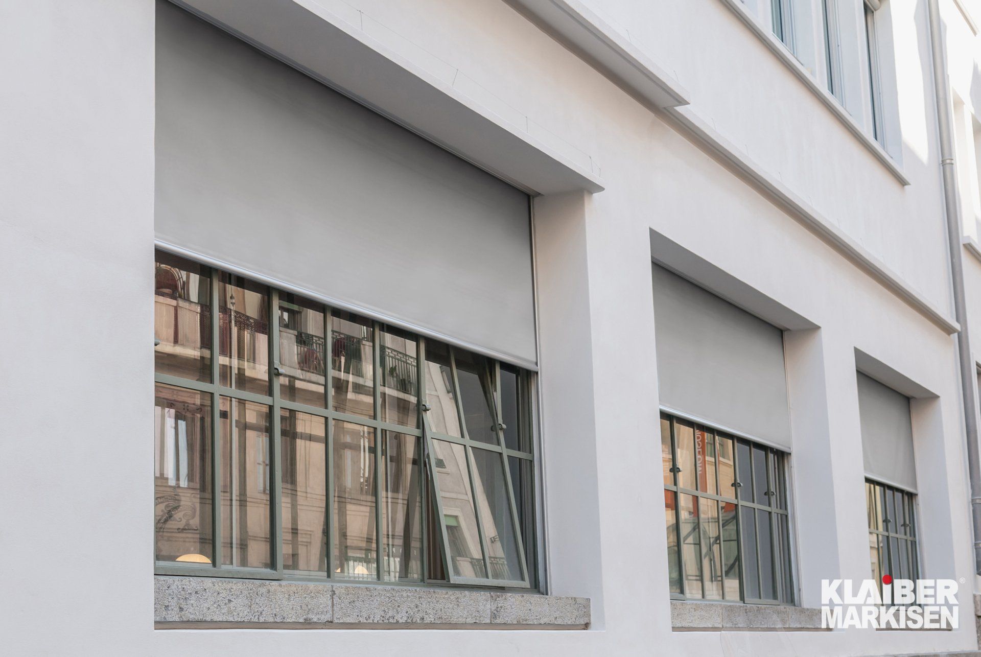 Klaiber Fassadenmarkise in grau vor Fenstern an Hauswand, halb heruntergelassen. LS Sonnenschutz Markisen mit Link zu Produktseite Fassadenmarkisen.