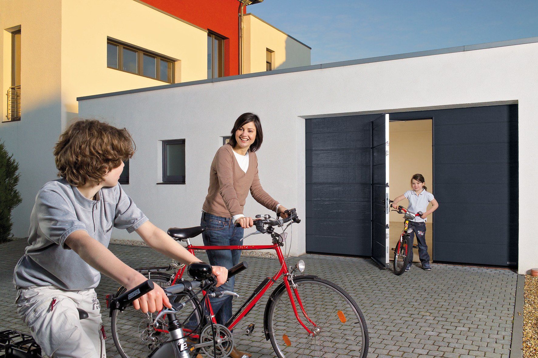 Kind kommt mit Fahrrad aus Schlupftür eines anthrazitfarbenem Sektionaltor