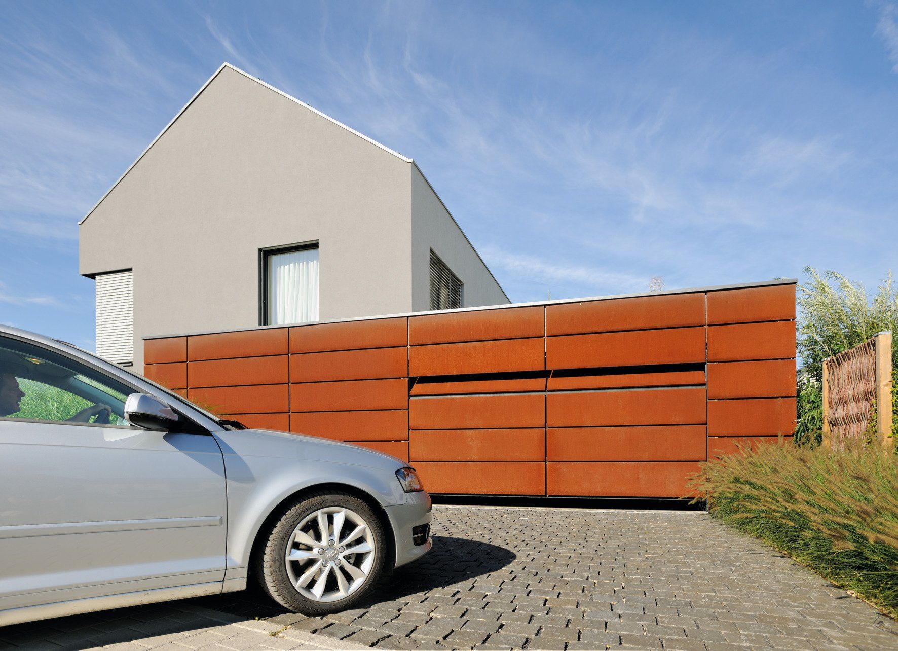 Garagentore oder Industrietore von Hoermann bei LS Sonnenschutz in Groß-Umstadt kaufen. Schutz und Sicherheit mit modernen schönen Designs. Wir beraten Sie gerne zu verschiedenen Modellen und Farben im Raum Darmstadt, Dieburg, Frankfurt, Aschaffenburg, Odenwald. Auto steht vor großer, sich öffnender Garage mit kupferfarbenen Blenden, Link zu Produktseite Garagentore und Industrietore