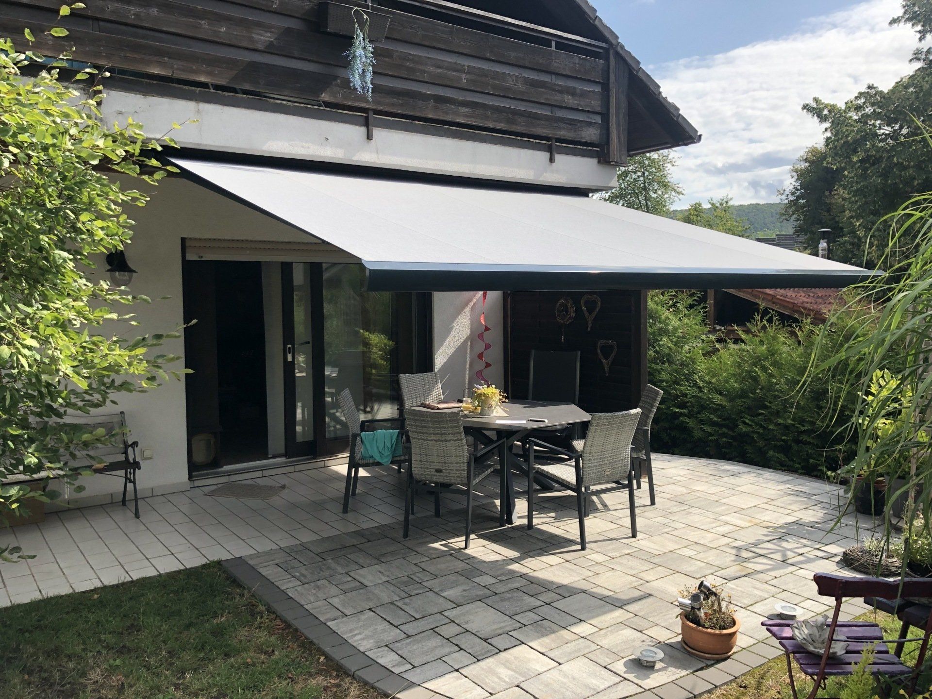 Referenzprojekt, ausgefahrene Kassettenmarkise mit grauem Stoff über Esstisch auf Terrasse, Ansicht von vorne