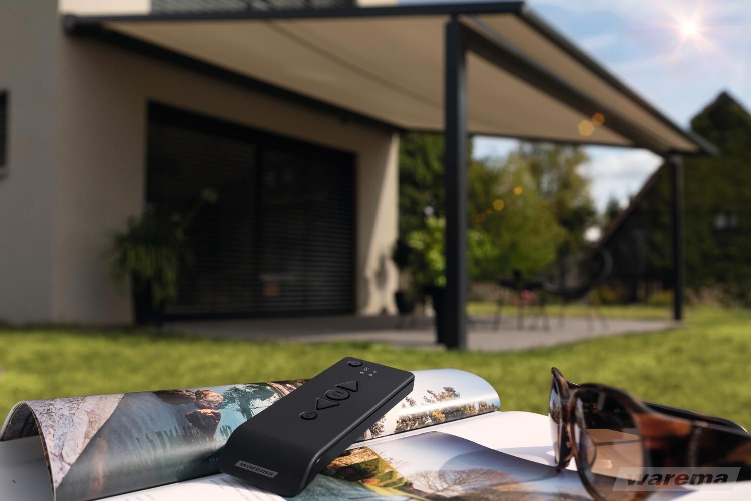 Markisenantrieb per Kurbel oder Motor. Funksteuerung für Markisen. LS Sonnenschutz Produktseite Markisen. Individuelle Markise kaufen bei LS Sonnenschutz in Groß-Umstadt.  Ausgefahrene Markise über Terrasse, auf einem Gartentisch liegt eine Fernbedienung, mit der die Markise gesteuert werden kann