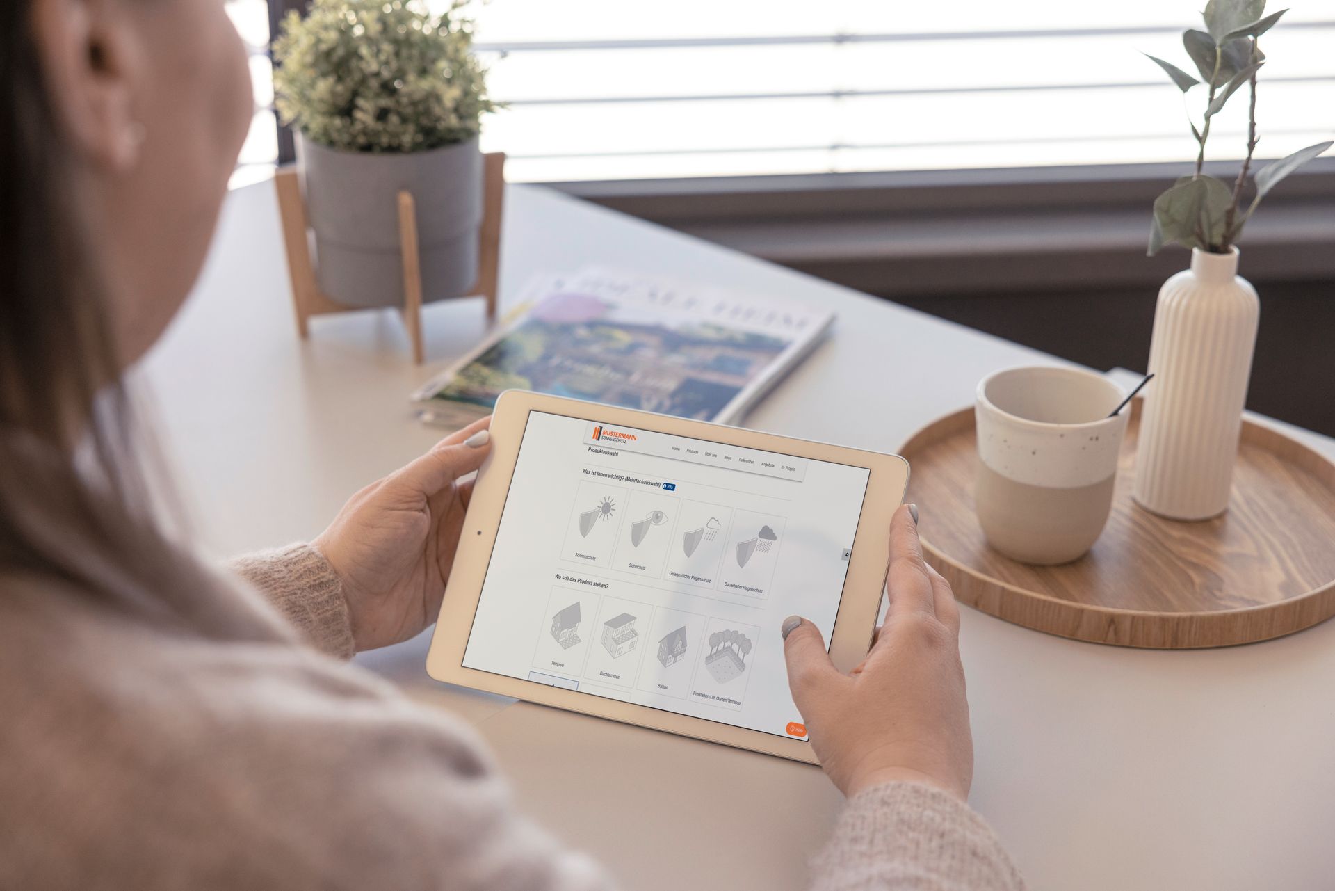 Frau sitzt an Tisch mit Tablet, auf dem der Digitale Kaufberater von Warema geöffnet ist, Link Kaufberater von Warema