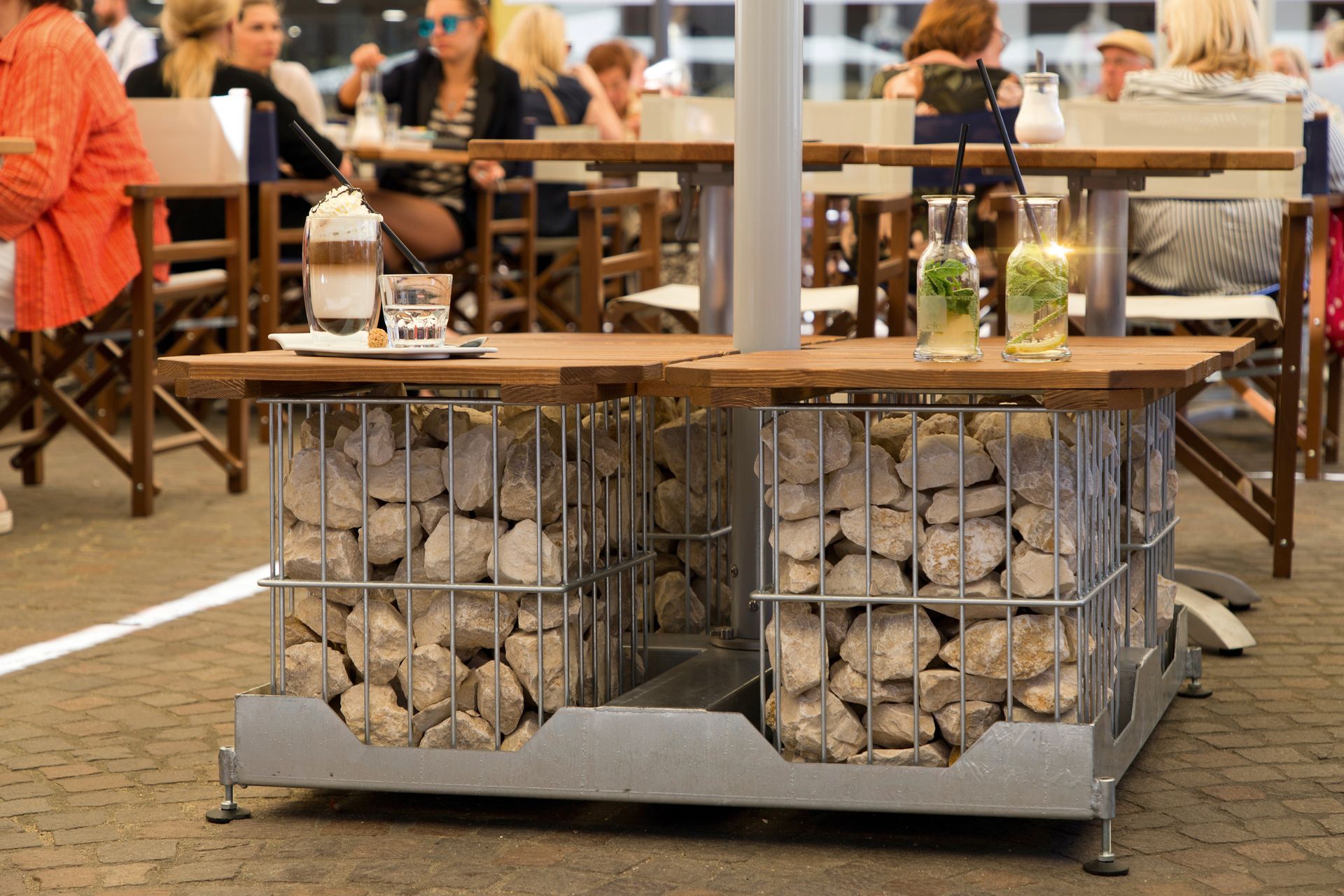 Schirmstaender Multicube von Caravita für die Gastronomie oder den privaten Gebrauch bei LS Sonnenschutz in Groß-Umstadt kaufen. Wir beraten Sie gerne zu verschiedenen Ausfuehrungen und Gestaltungsmoeglichkeiten im Raum Darmstadt, Dieburg, Frankfurt, Aschaffenburg, Odenwald. Caravita Schirmständer Multicube mit Holzauflage und hellen Bruchsteinen befüllt