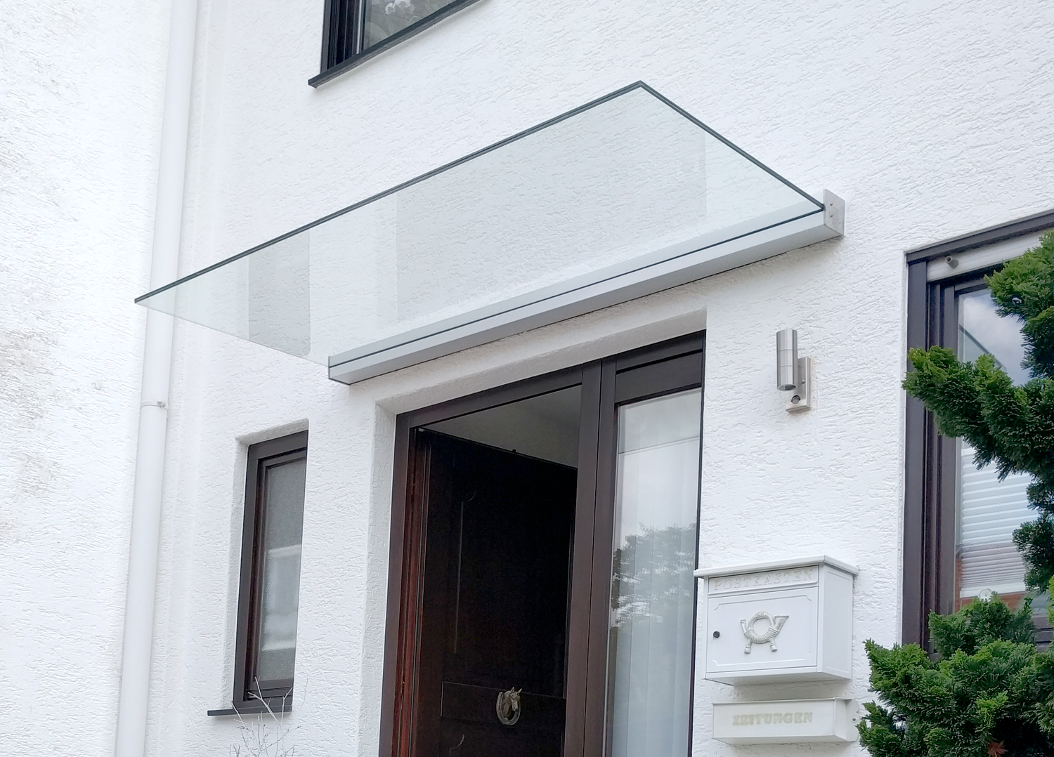 Panther Glas Vordach Plan Five für Ihren Eingangsbereich bei LS Sonnenschutz in Groß-Umstadt kaufen. Wir beraten Sie gerne zu verschiedenen Ausführungen und Modellen im Raum Darmstadt, Dieburg, Frankfurt und Rhein-Main Gebiet, Aschaffenburg, Odenwald. Panther Glas Plan Five Glasdachsystem montiert über Haustür mit weißem Aluminium-Wandklemmprofil passend zur weißen Fassade
