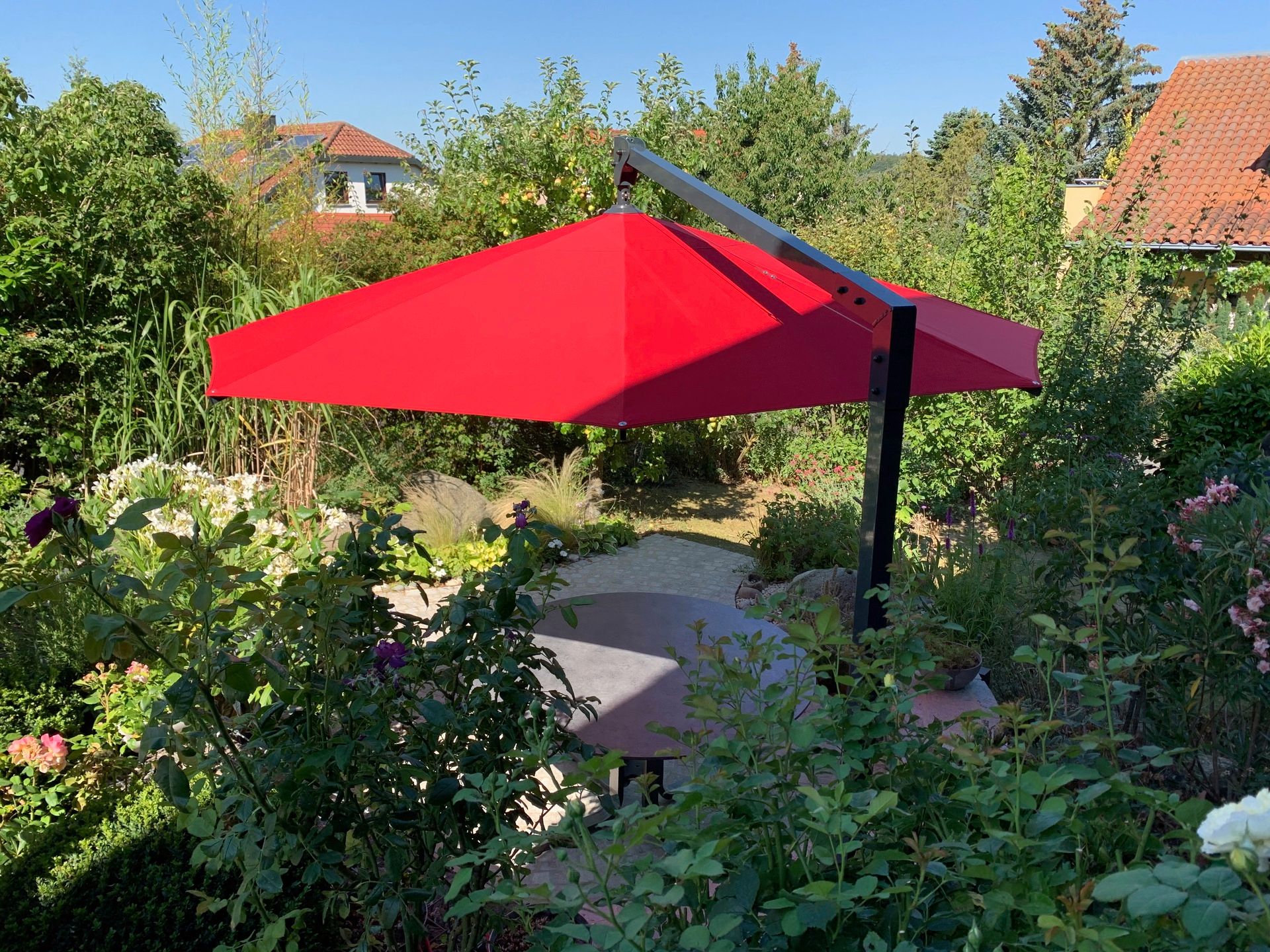 Caravita Sonnenschirme Amalfi mit roter Tuchbespannung ueber einer kleinen Sitzecke in einem Garten. LS Sonnenschutz Produktseite Sonnenschirme.