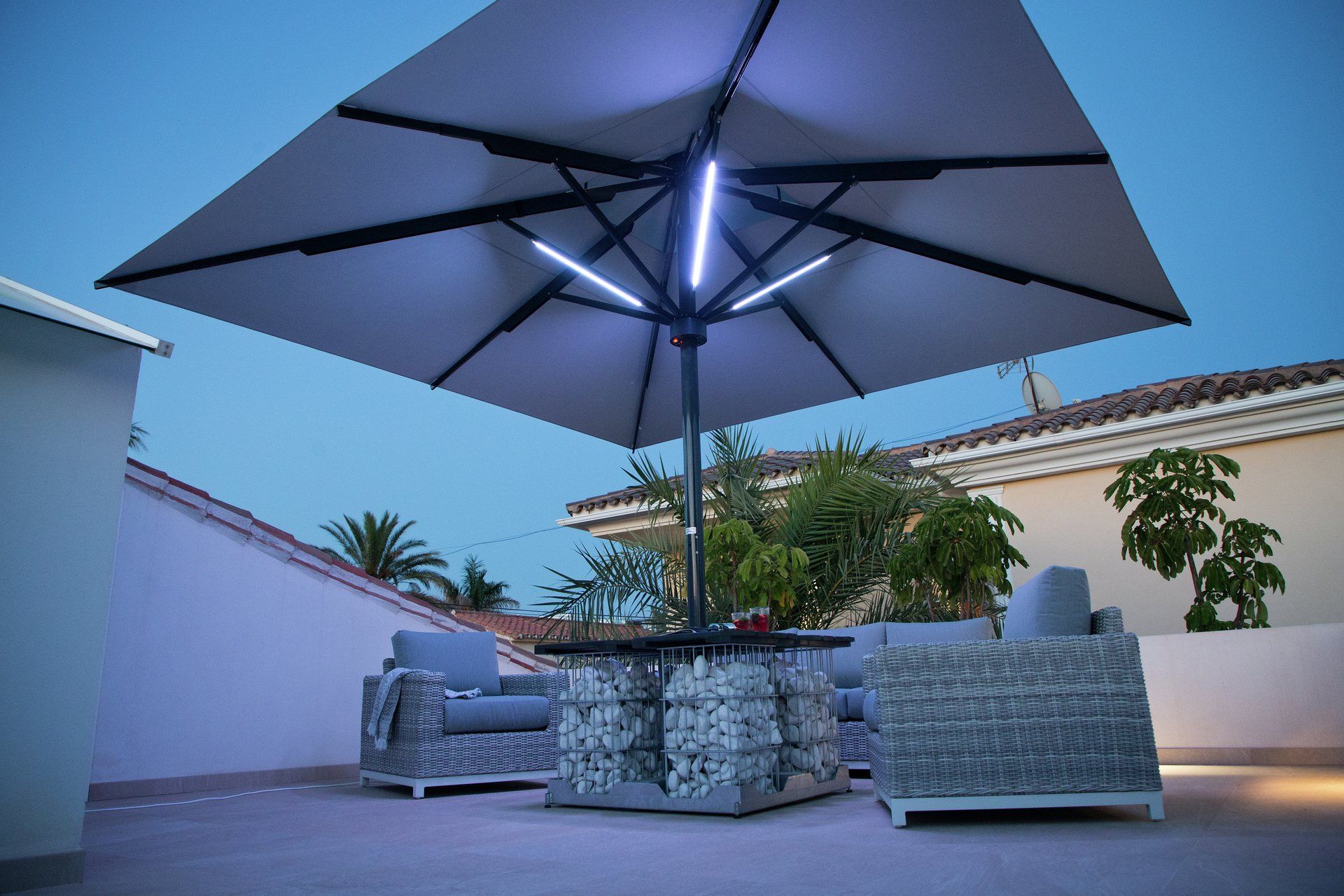 Caravita Sonnenschirm Big Ben Freestyle ausgefahren in der Dämmerung mit LED Lichtern an den Streben, Ständer als Tisch
