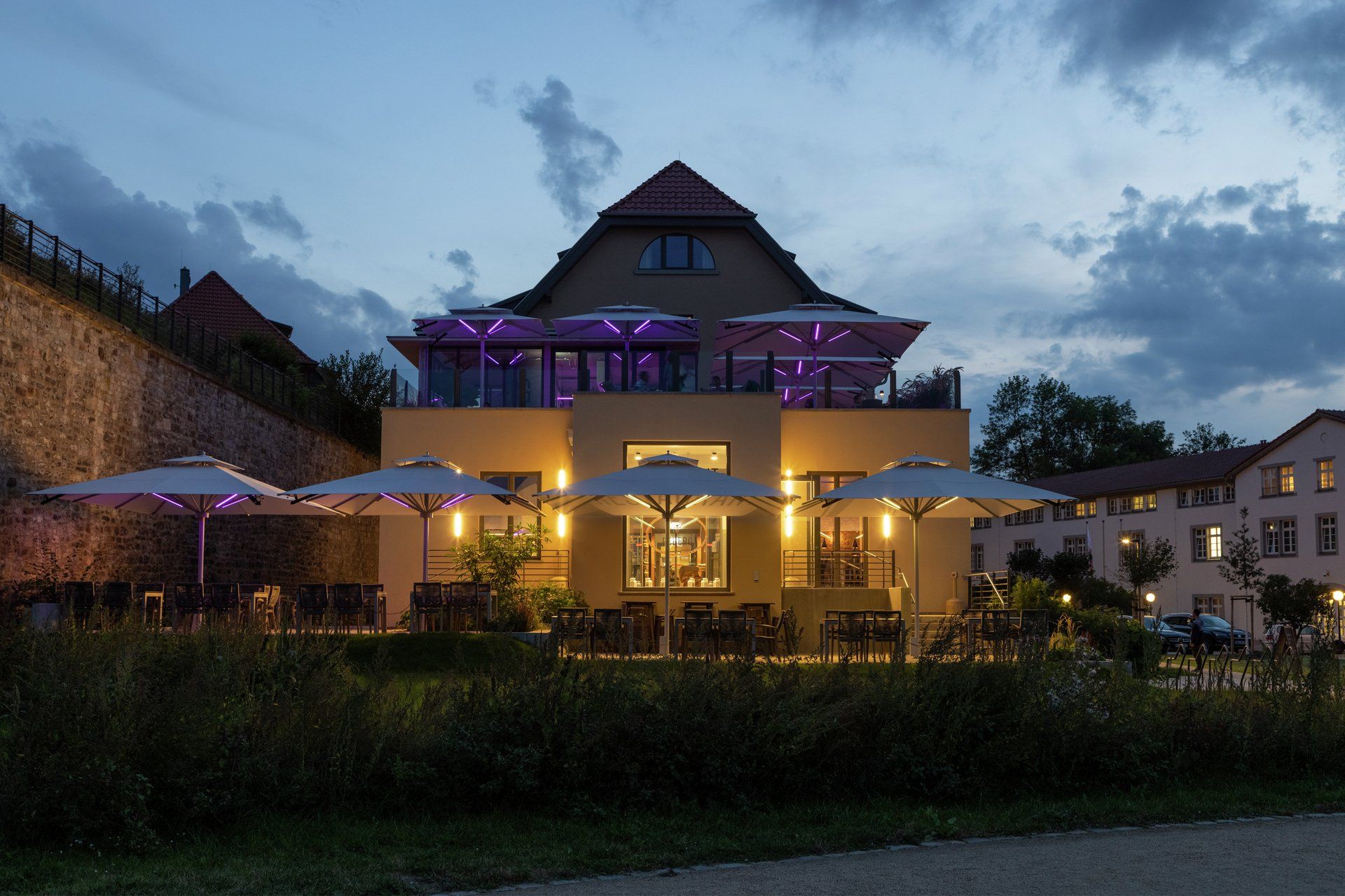 Sonnenschirm Big Ben von Caravita mit integriertem LED-Strebenlicht Beleuchtung für Gastronomie, Balkon oder Terrasse bei LS Sonnenschutz in Groß-Umstadt kaufen. Wir beraten Sie gerne zu verschiedenen Modellen und Farben im Raum Darmstadt, Dieburg, Frankfurt, Aschaffenburg, Odenwald. Mehrere Caravita Sonnenschirme Big Ben mit integriertem LED-Strebenlicht aufgestellt auf Balkon und Terrasse eines Restaurants. Foto zur Daemmerung. LS Sonnenschutz Produktseite Sonnenschirme.