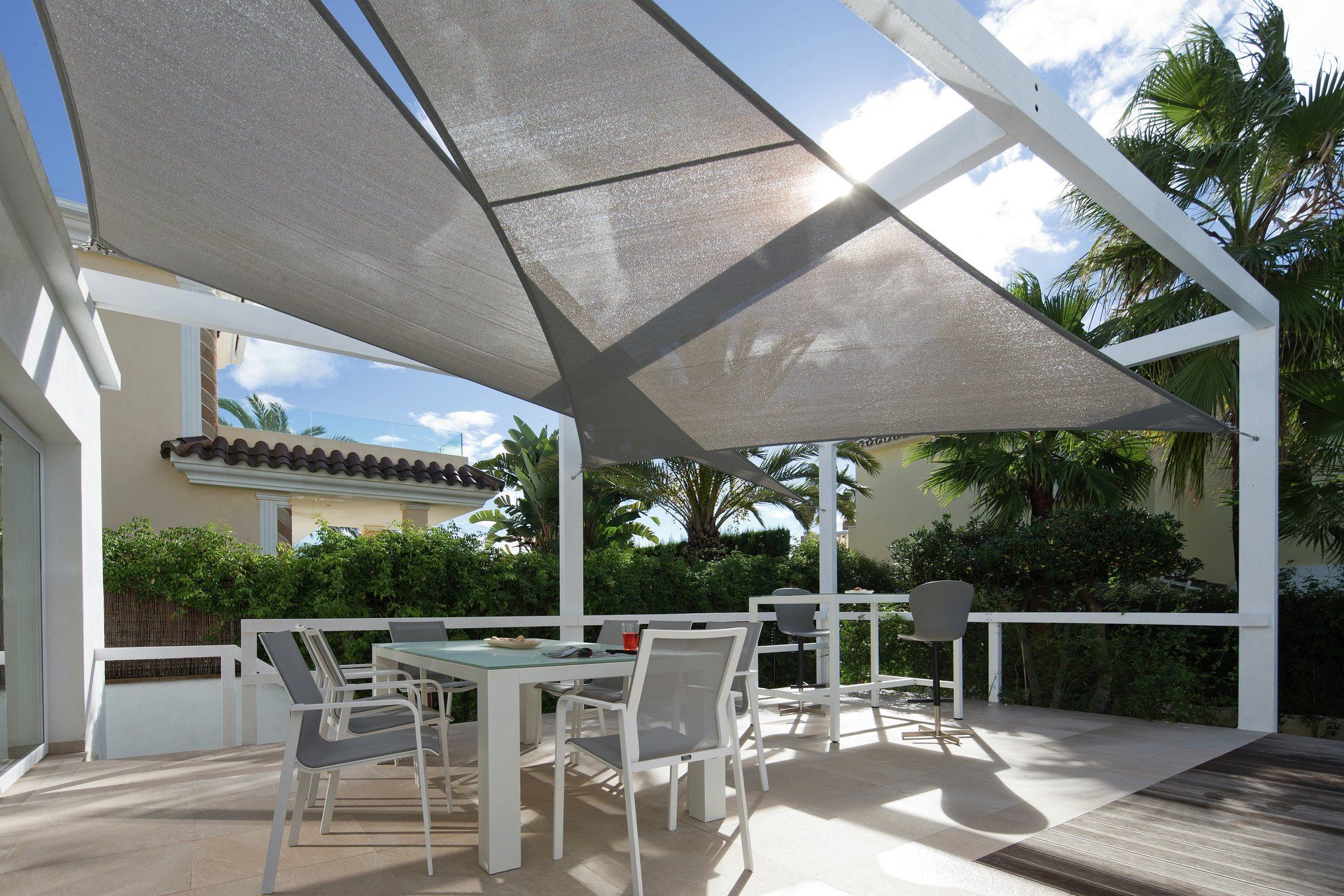 Caravita Sonnensegel für Balkon oder Terrasse bei LS Sonnenschutz in Groß-Umstadt kaufen. Leichter Sonnenschutz und stylisches Designelement mit Urlaubsatmosphäre. Wir beraten Sie gerne zu verschiedenen Modellen und Farben im Raum Darmstadt, Dieburg, Frankfurt, Aschaffenburg, Odenwald. Ansicht von unten auf zwei sich ueberlappende graue Caravita Sonnensegel ueber Terrasse mit Konstruktion bespannt bei prallem Sonnenschein spendet Schatten ueber Sitzbereich. LS Sonnenschutz Produktseite Sonnensegel.