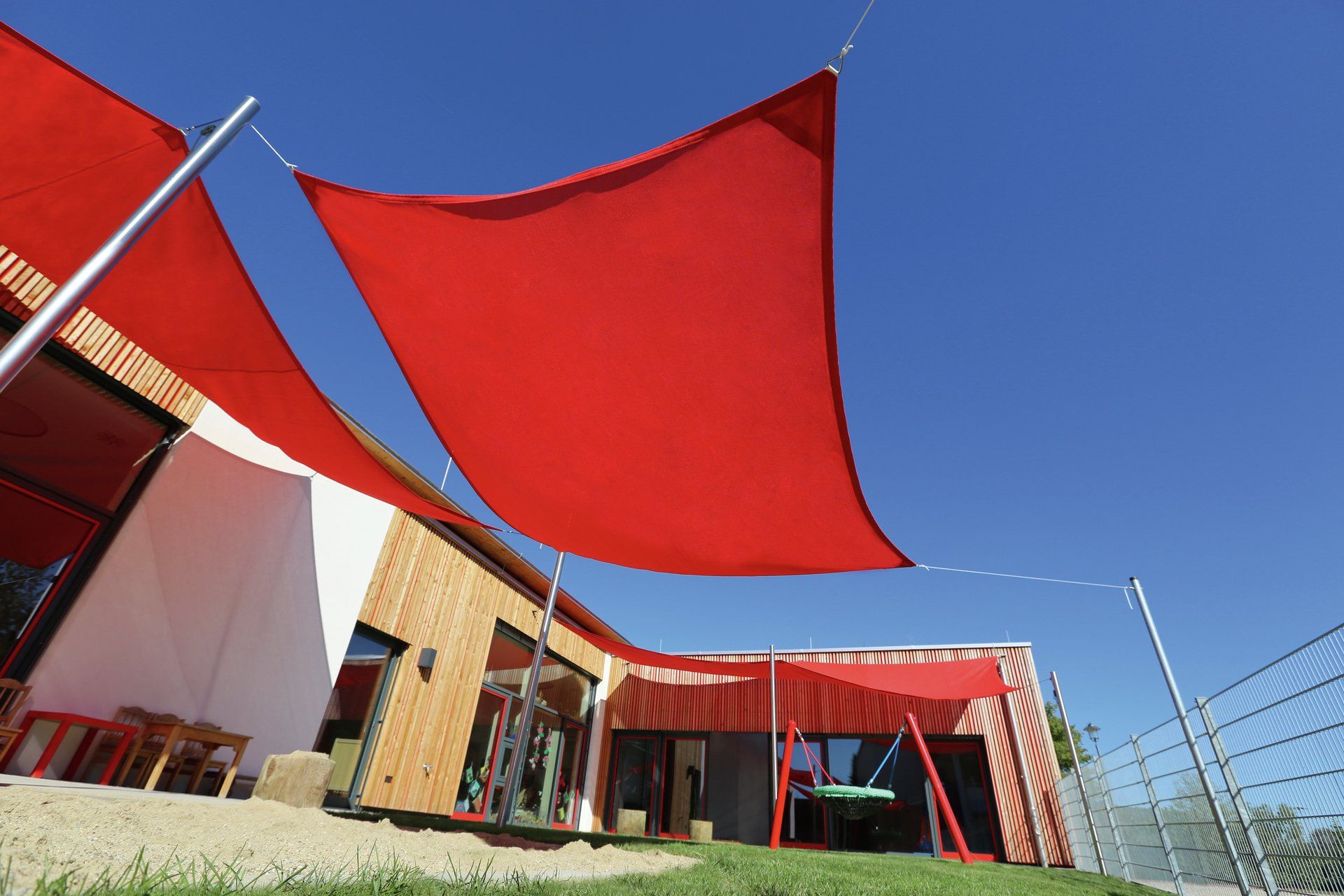 Caravita Sonnensegel für Balkon oder Terrasse bei LS Sonnenschutz in Groß-Umstadt kaufen. Sonnensegel All Season perfekt als ganzjähriger Sonnenschutz für große Flächen. Ideal für Kindergarten und Spielplatz. Wir beraten Sie gerne zu verschiedenen Modellen und Farben im Raum Darmstadt, Dieburg, Frankfurt, Aschaffenburg, Odenwald. Drei rote Caravita Sonnensegel freistehend und an Hauswand befestigt im Kindergarten über Sandkasten gespannt