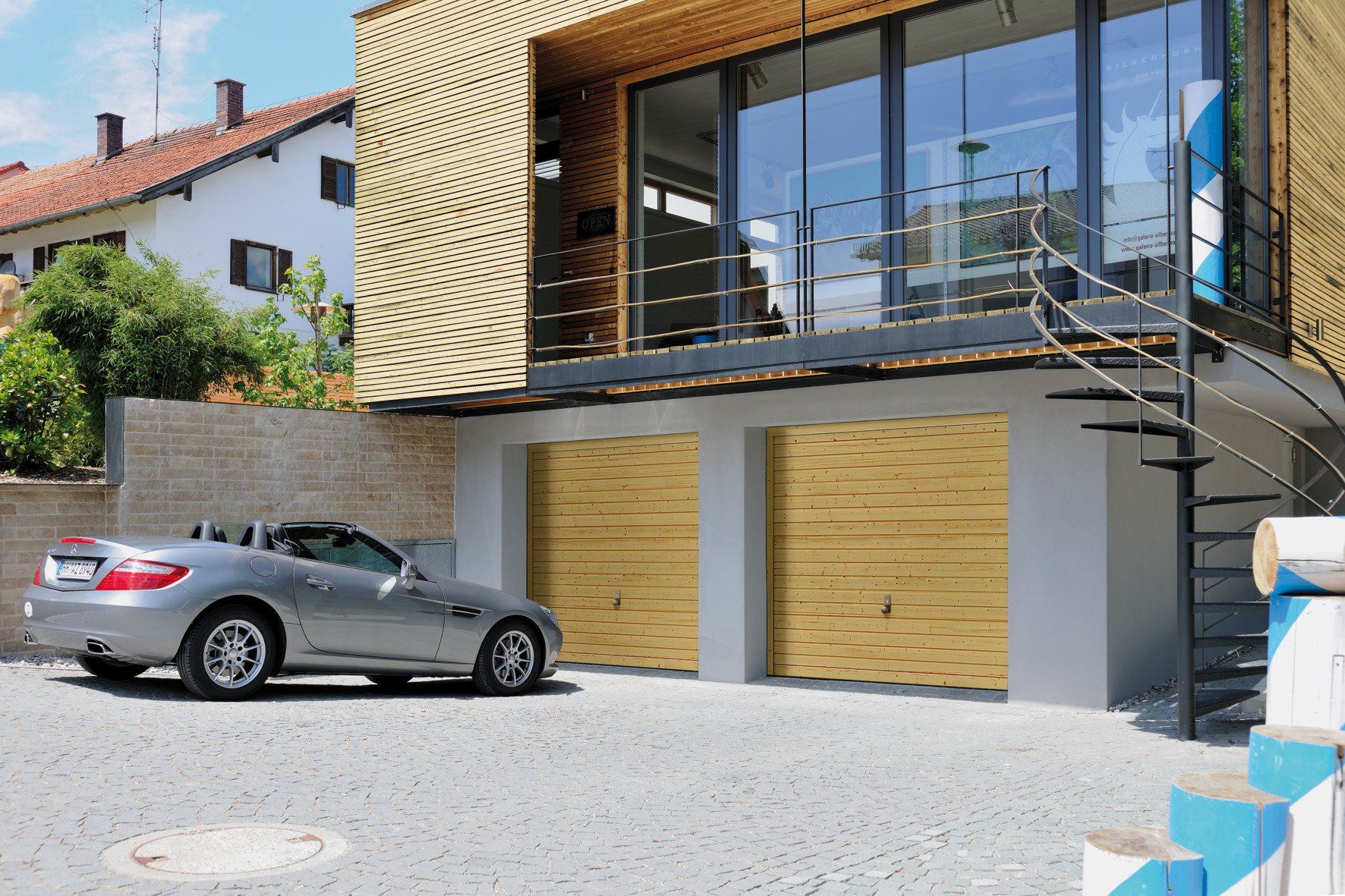 Modernes Haus, silbernes Auto steht vor einer der zwei Garagen mit Holzlamellenoptik, Garagentore geschlossen
