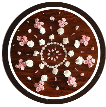 Mandala aus weissen und rosa Blüten auf dunklem Holz