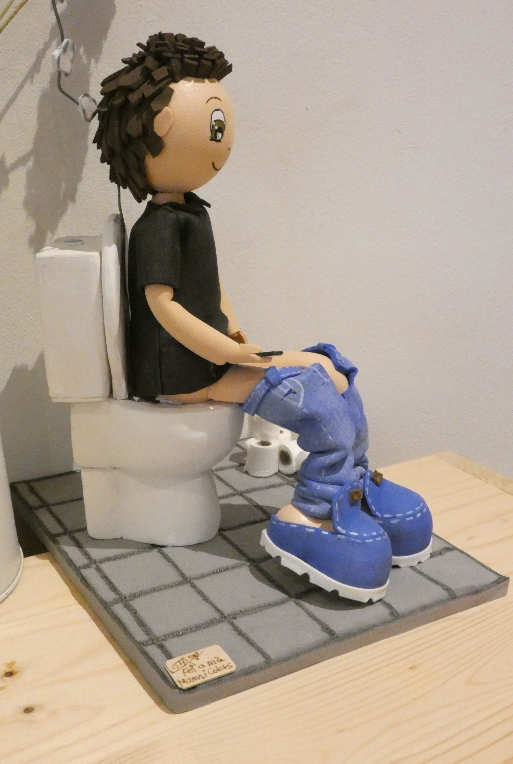 fofuchas personalizadas,
Fofucha hombre sentada en el wc, con el movil en la mano y mirando los whatsapp, tiene los rollos de papael wc en el suelo.