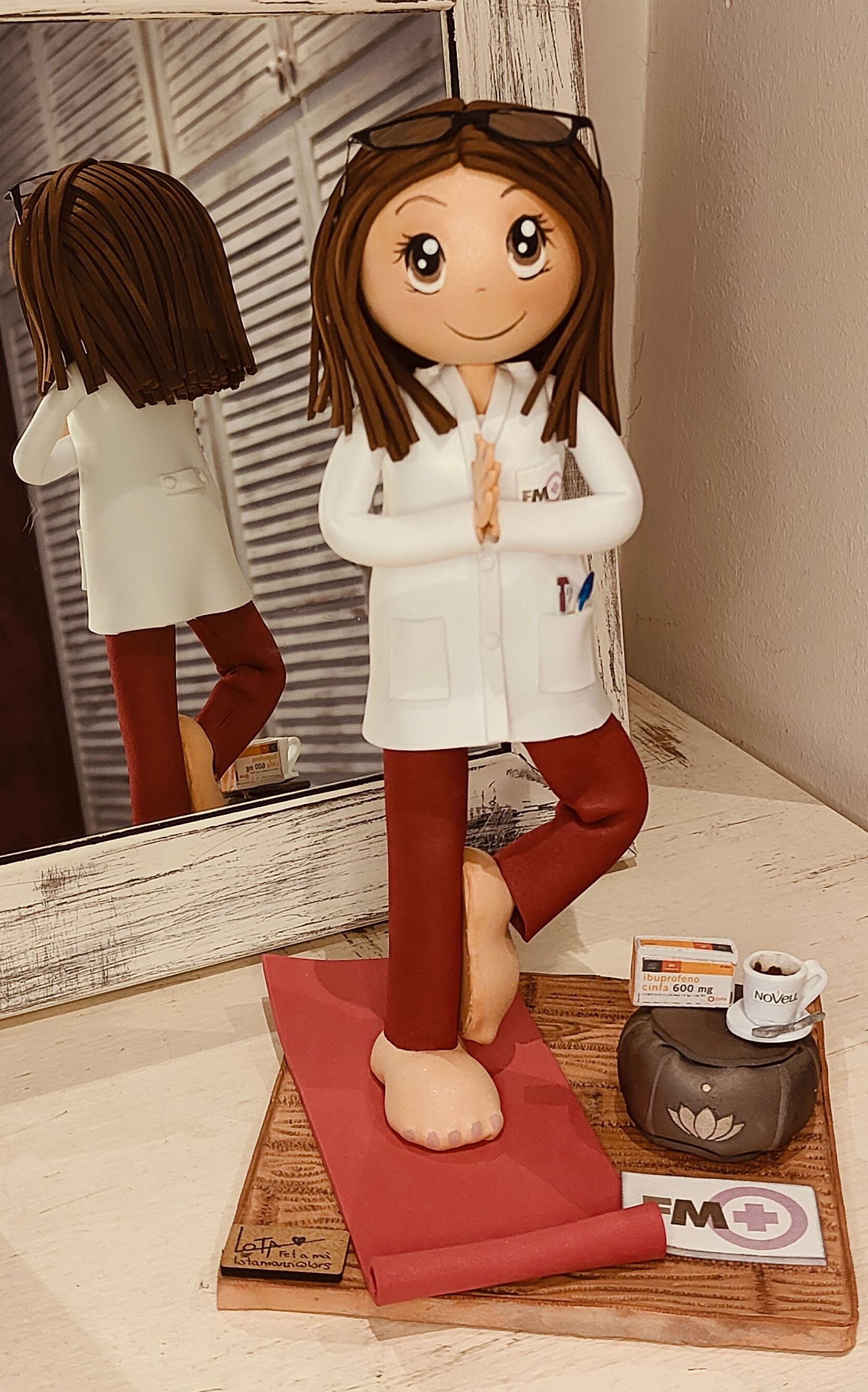 Fofuchas personalizadas de farmacéutica haciendo yoga.
Vestida con una bata blanca, y pantalón granate, descalza sobre una colchoneta de yoga, cojín zen y sobre el una taza de café
