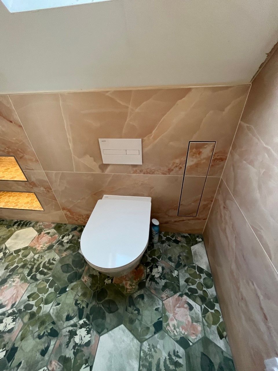 Toilet in a bathroom with gloss rosa sapphire and green decor floor tiles