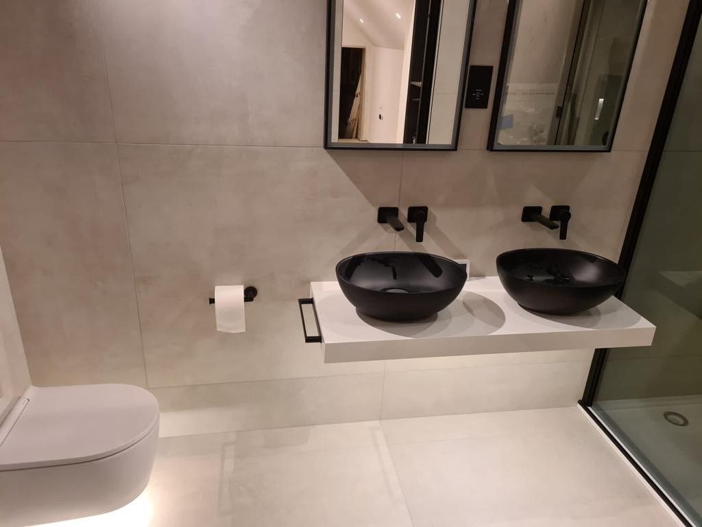 MIlan ivory on the floors and wall of the bathroom with black sinks and tinted black shower glass