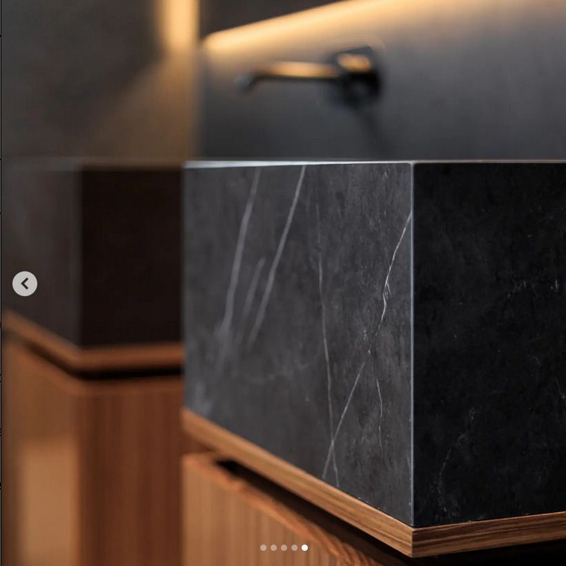 Close-up of a black marble basin sink, showcasing the sleek lines and natural stone texture, illuminated by ambient lighting.