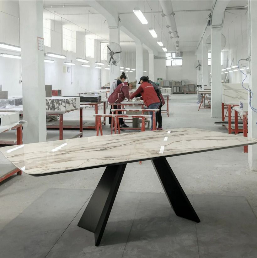 A marble tabletop in a manufacturing workshop, with workers crafting stone furniture pieces in the background.