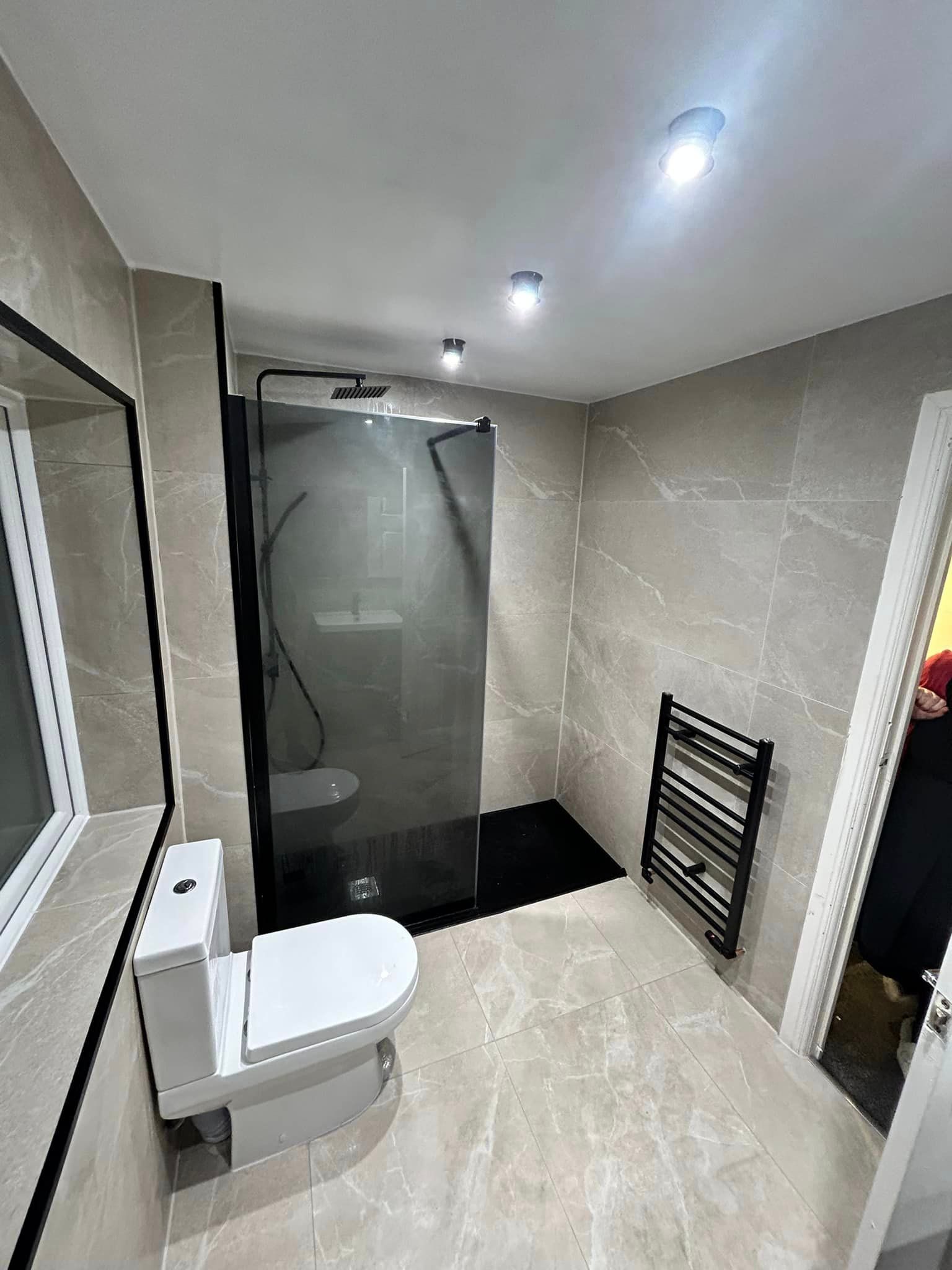 Room shot of a modern bathroom with tinted glass and a black towel rack with marble effect tiles used on the walls
