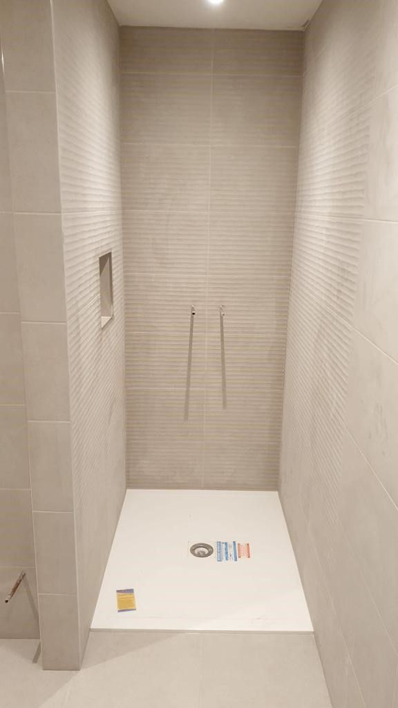 A sleek modern shower area with beige textured tiles. A minimalist design with recessed shelving and polished metal fixtures completes the look.