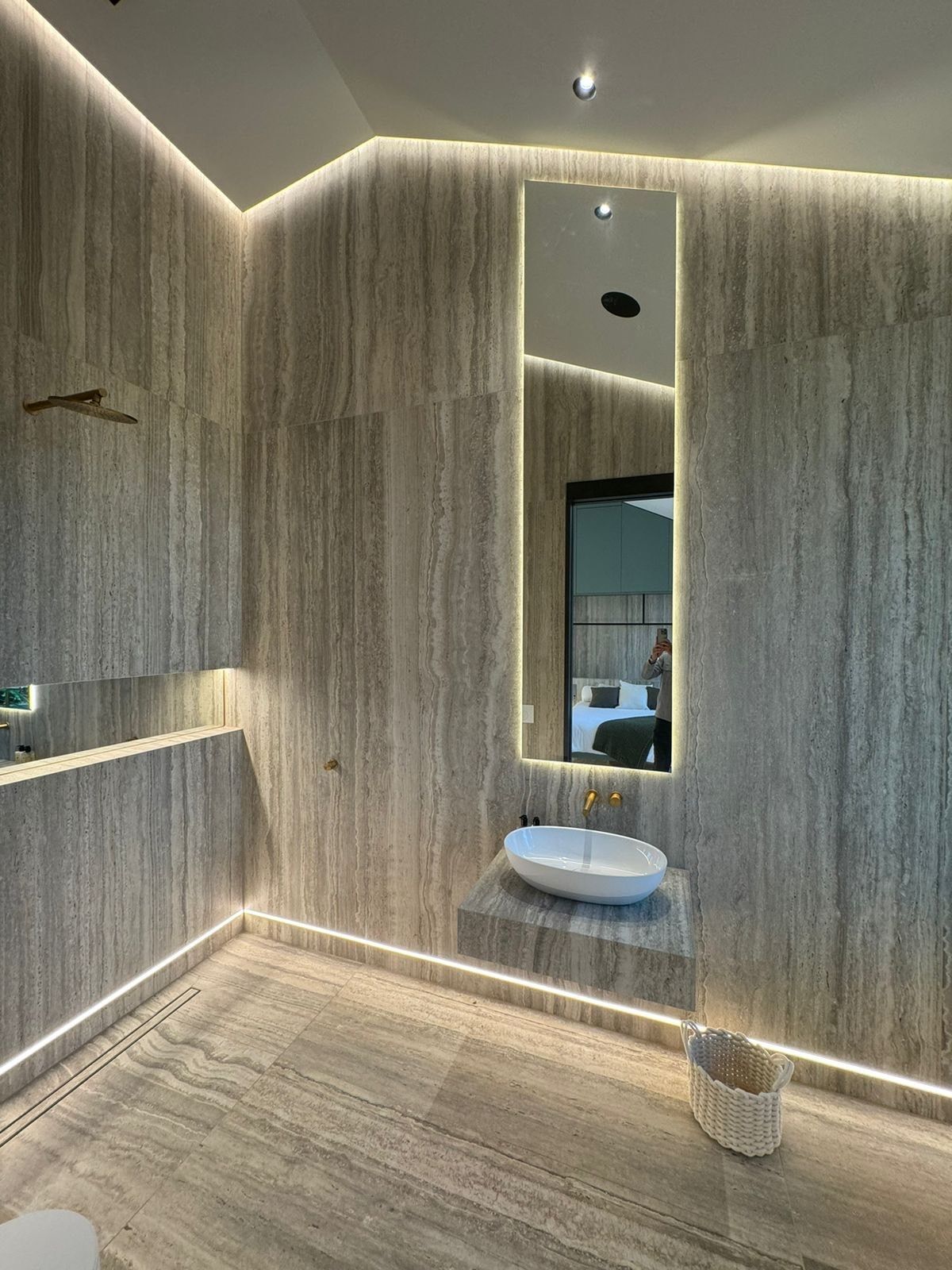 Modern bathroom with travertine wall tiles and led lights around the room and mirror