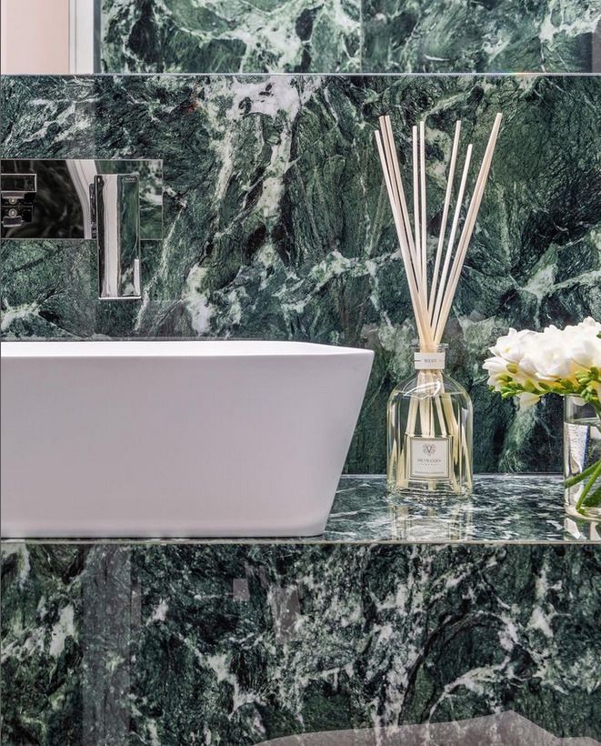 A luxurious bathroom with striking green marble tiles, complemented by a white bathtub and decorative reed diffuser.