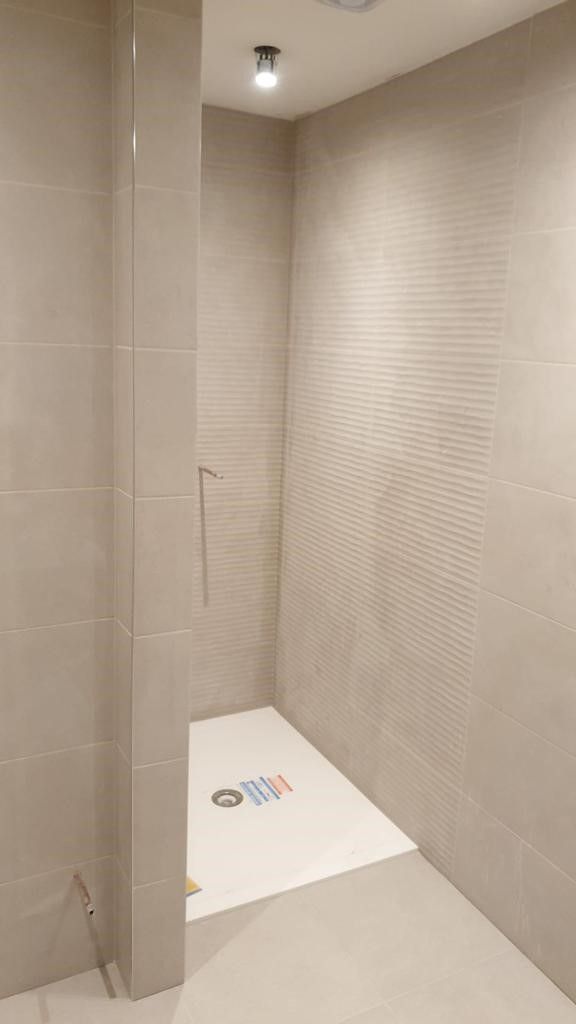 A clean and modern shower space with beige ribbed tiles on the walls and a white shower tray. Recessed lighting adds to the minimalist aesthetic.