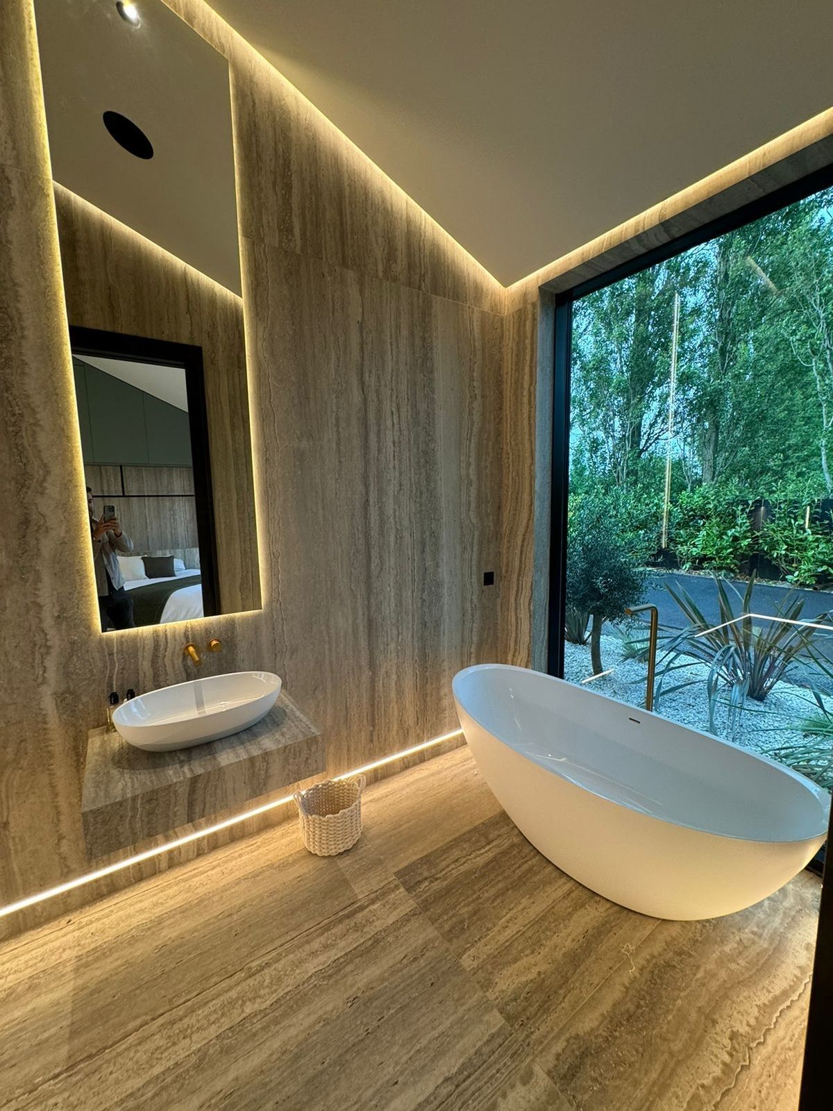 Room shot of modern bathroom with travertine wall and floor tiles and a white bath
