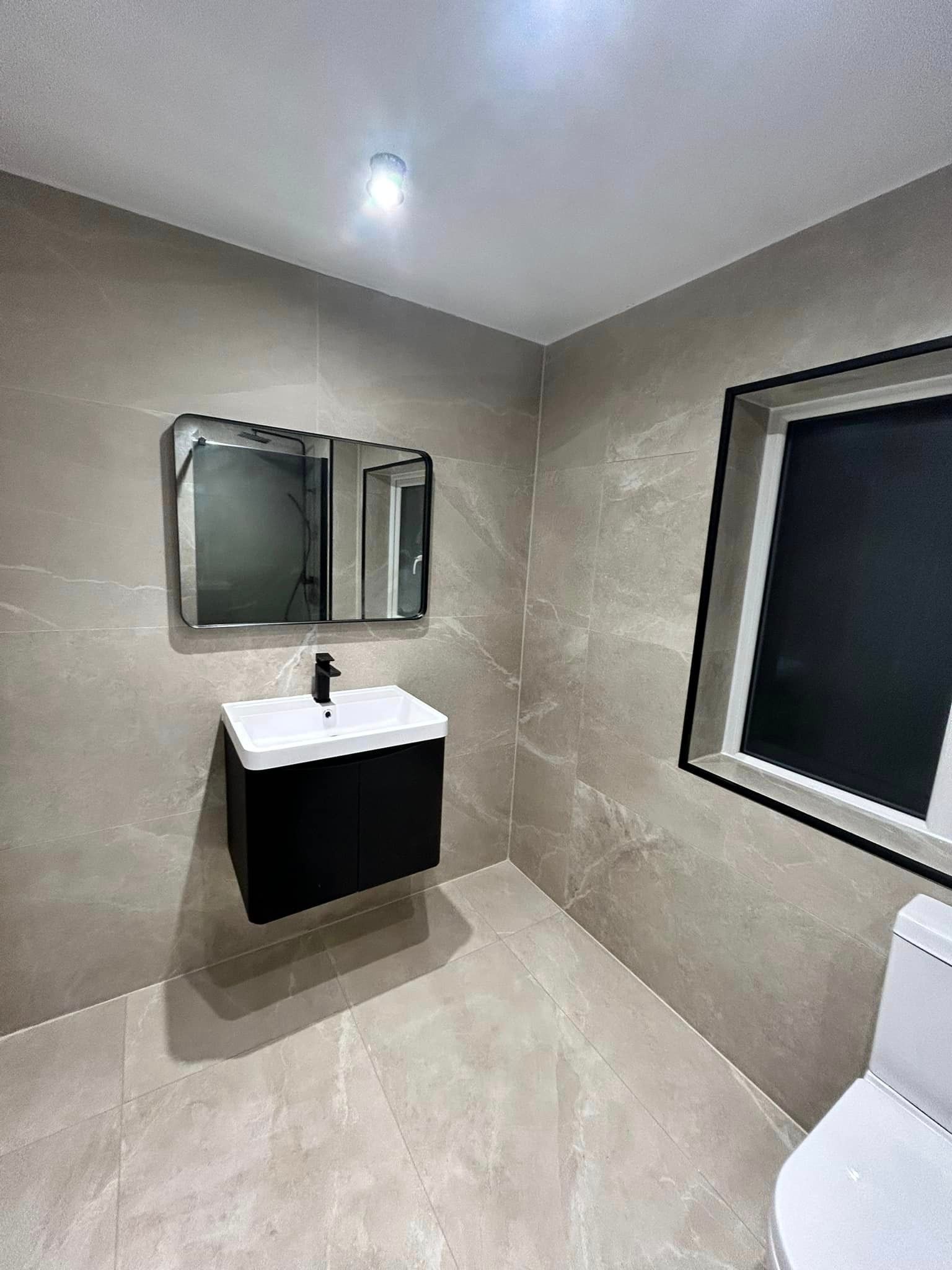 Black themed bathroom with grey marble wall tiles featuring a black sink with a black faucet