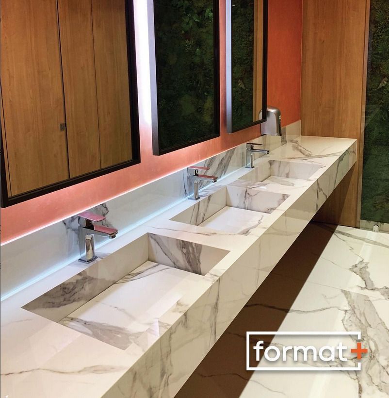 A row of elegant marble sinks with modern faucets in a public washroom, framed by glowing backlit mirrors and wooden accents.A row of elegant marble sinks with modern faucets in a public washroom, framed by glowing backlit mirrors and wooden accents.