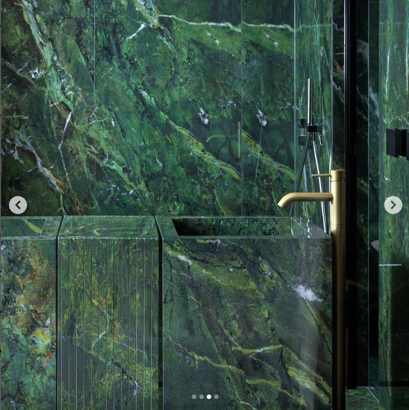 A bathroom with a bold green marble vanity and wall tiles, accentuated by gold fixtures and a contemporary design.