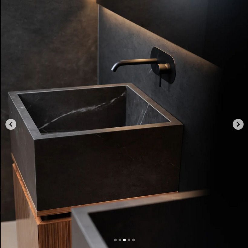 A black square stone basin sink with a matte black wall-mounted faucet, set in a moA luxurious bathroom with striking green marble tiles, complemented by a white bathtub and decorative reed diffuser.ody, modern bathroom.