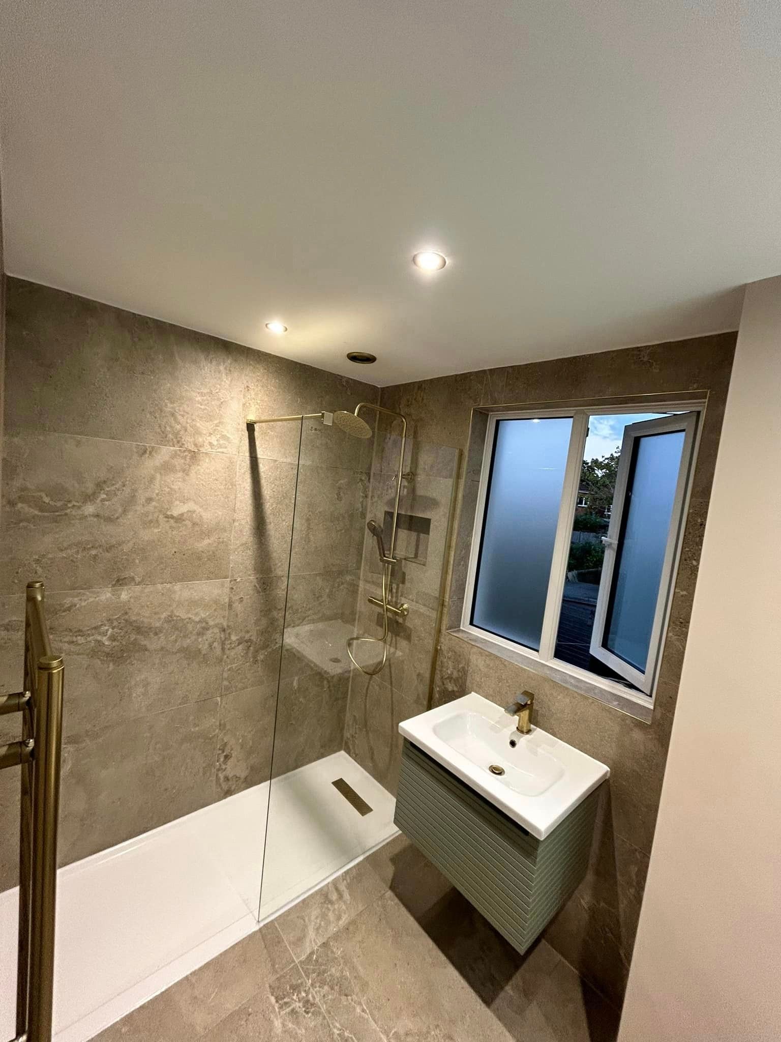 Standing shower and a limestone effect tiled wall in a bathroom with frosted windows