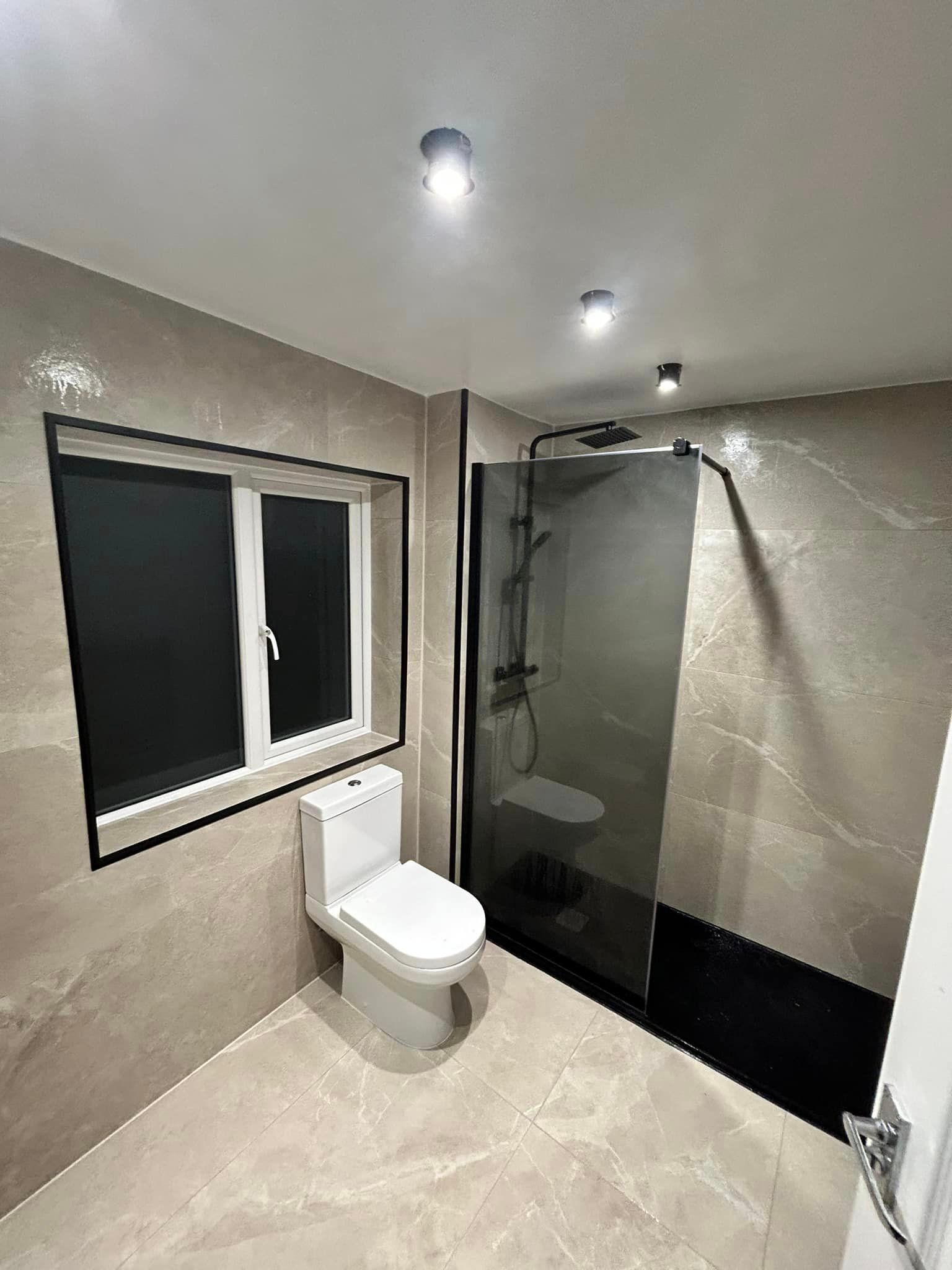 TInted black shower glass with blackout windows and marble effect wall tiles in this bathroom
