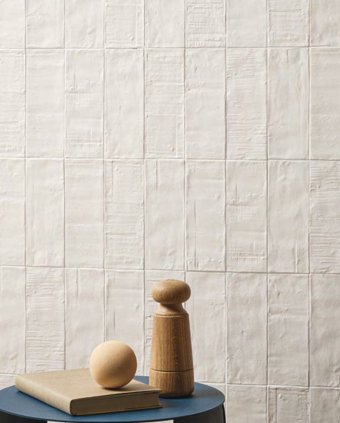 Textured white wall tiles in a rectangular format, paired with minimal wooden decor, including a round ball and a salt shaker-like object on a dark blue circular table.