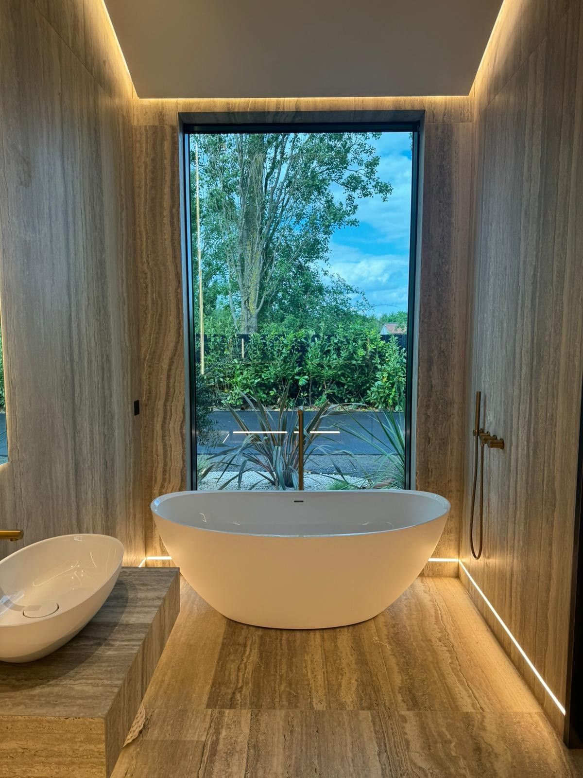 bathroom with big glass pane Infront of the bath travertine wall tiles