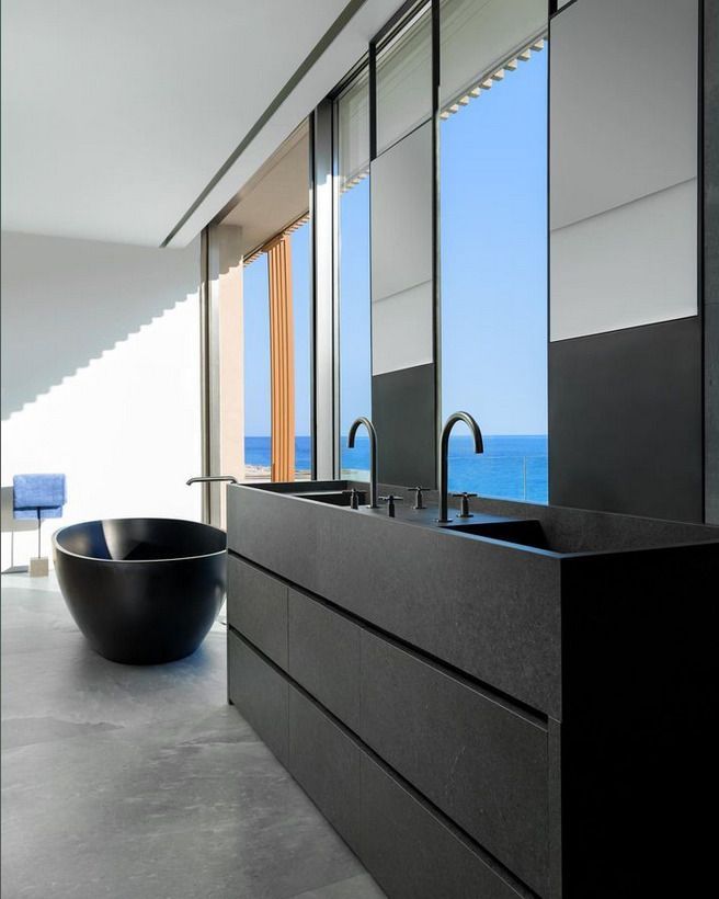 A sleek black modern bathroom featuring a dual-sink vanity and floor-to-ceiling windows overlooking a sea view, with a freestanding black bathtub.