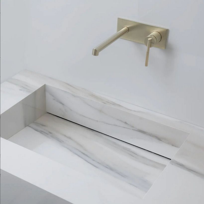 Elegant white marble sink with straight lines, paired with a matte gold wall-mounted faucet, offering a minimalistic design.