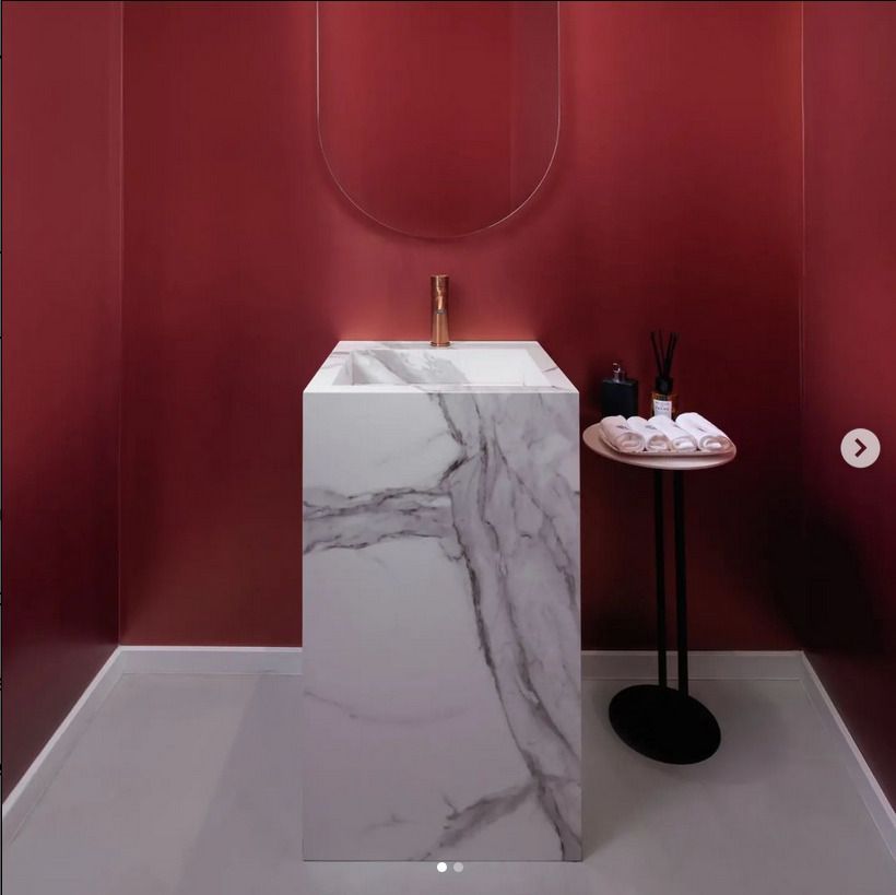 A striking minimalist bathroom with a white marble sink set against a red accent wall, complemented by a modern copper faucet.