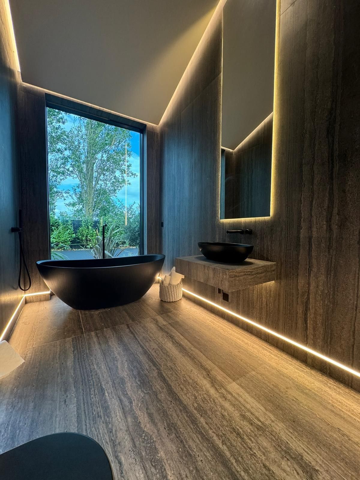 Black sink and black bath with travertine wall tiles and floor tiles