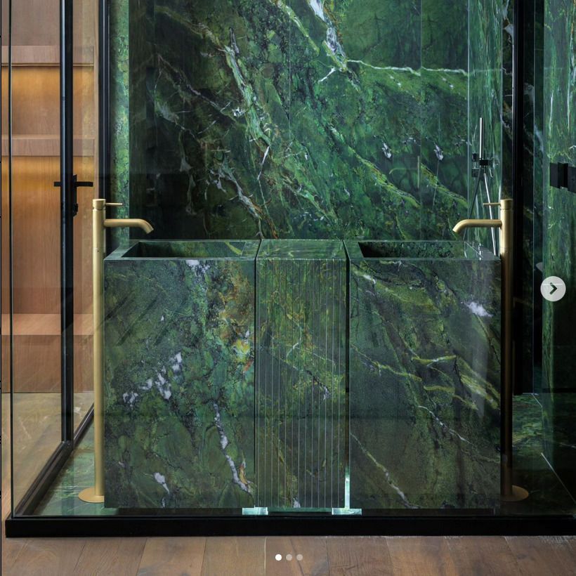 A bathroom with a green marble countertop and sinks, accented with gold faucets. The green marble extends to the walls, creating a bold and opulent space.