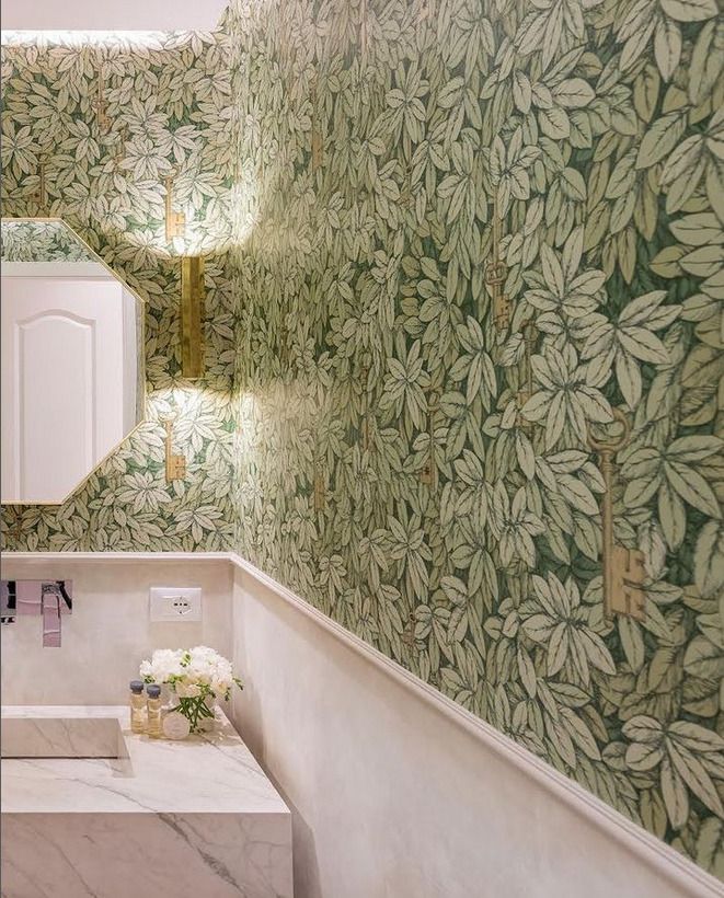 A small powder room with a vibrant green leaf-patterned wallpaper, accompanied by a sleek white marble vanity and minimalist decor.