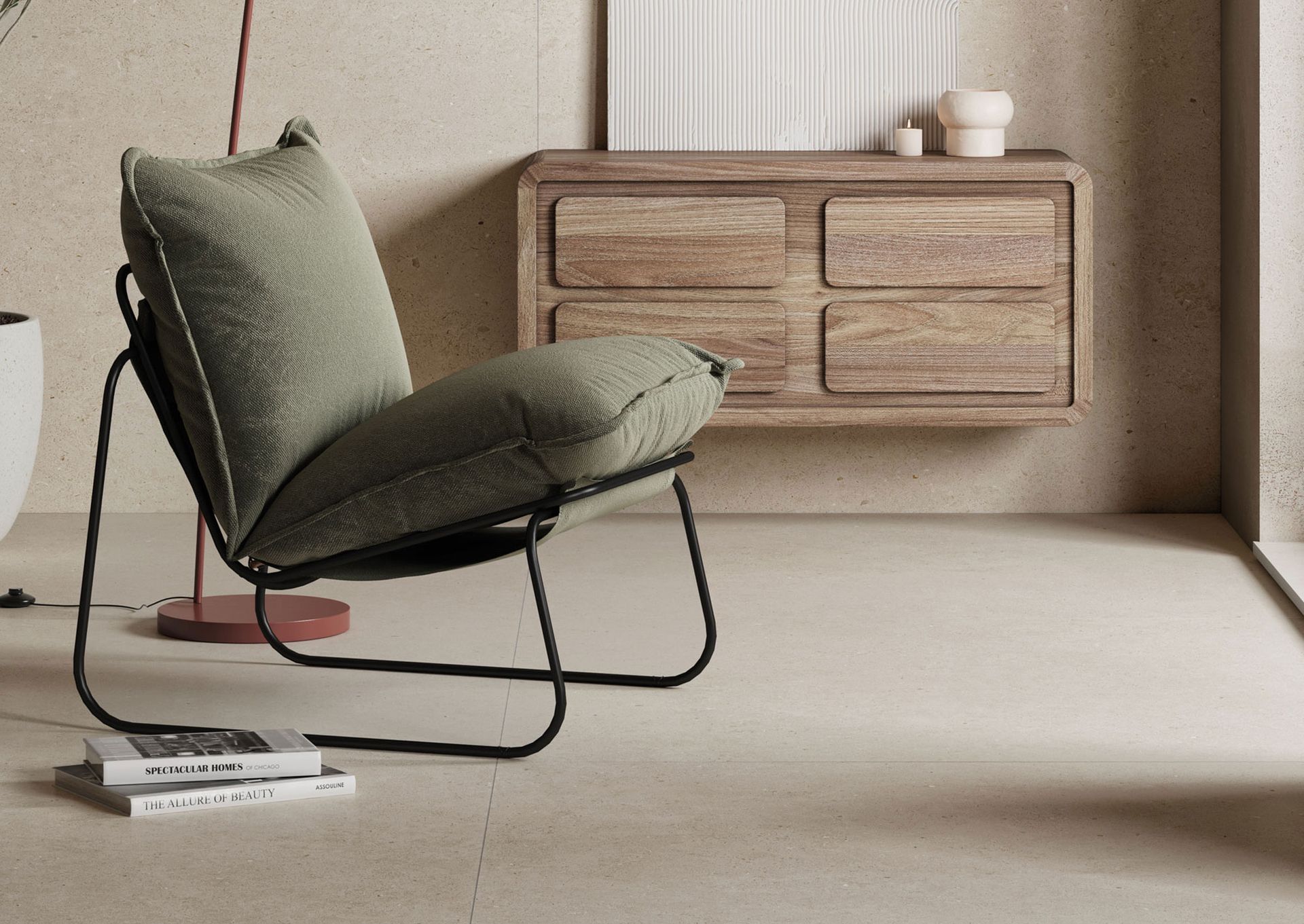 Cozy and modern interior featuring a comfortable lounge chair with a black metal frame and plush olive-green cushions. The chair is placed near a wooden wall-mounted cabinet with a unique rounded design and smooth finishes. The light beige stone tile flooring adds to the clean and minimalistic aesthetic. A small stack of coffee table books rests on the floor, adding a casual and inviting touch. A potted plant and a few decorative items on the cabinet enhance the natural and serene atmosphere of the space.