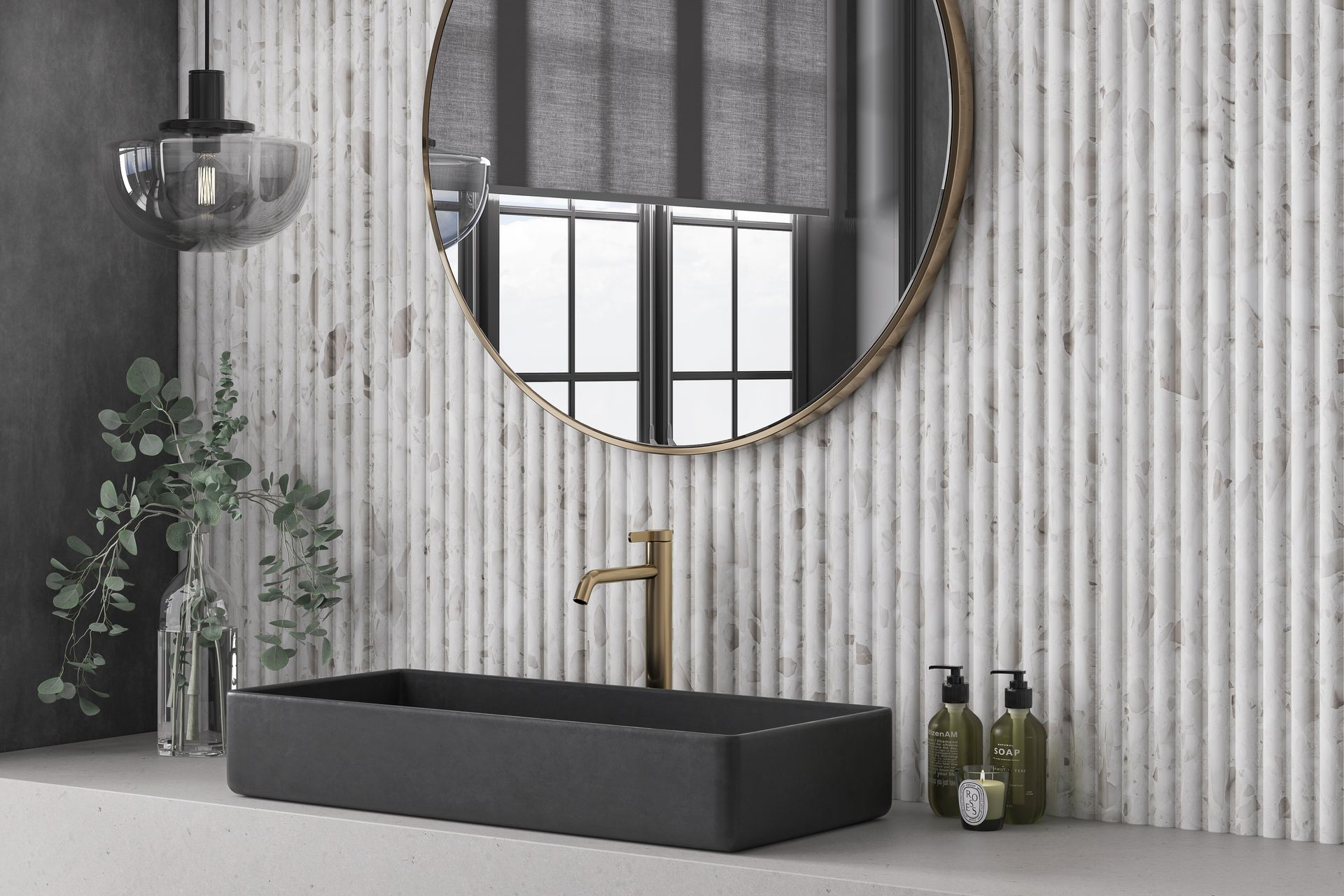 A stylish bathroom with a white fluted terrazzo wall, modern black basin, gold tap, and decorative eucalyptus in a glass vase. A large round mirror reflects the room’s elegance