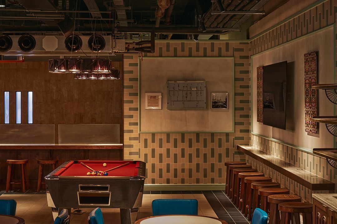 pool table with mosaic tile wall behind it with stools all around