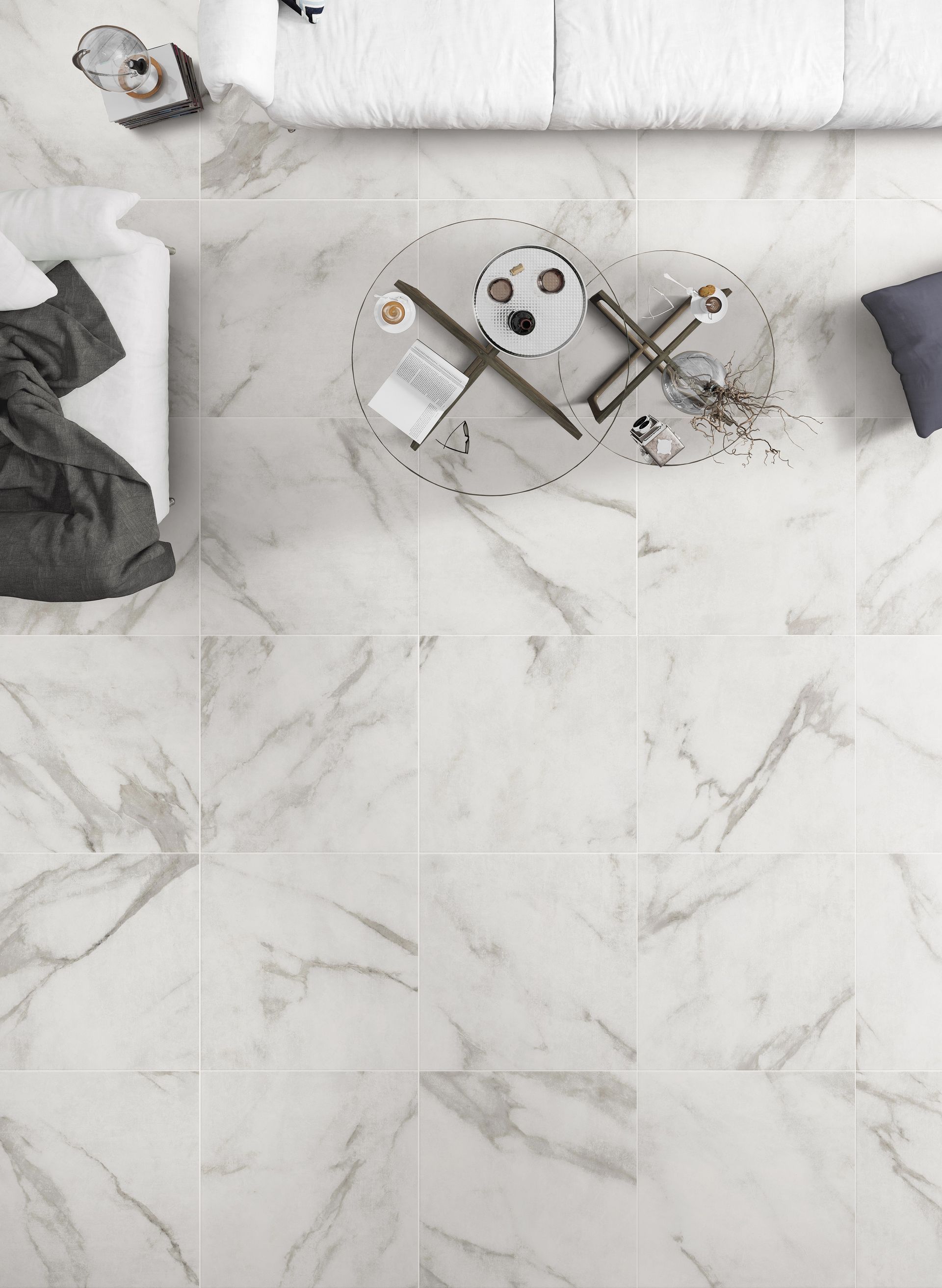 Overhead view of a modern living room featuring elegant white marble tiles with subtle grey veining. The room includes a sleek glass coffee table with a bronze-colored metal base, holding a vase, books, and decorative items. The surrounding area has white sofas with a plush, inviting look, complemented by a grey throw blanket. The clean lines and minimalistic decor emphasize the room's sophisticated and airy atmosphere