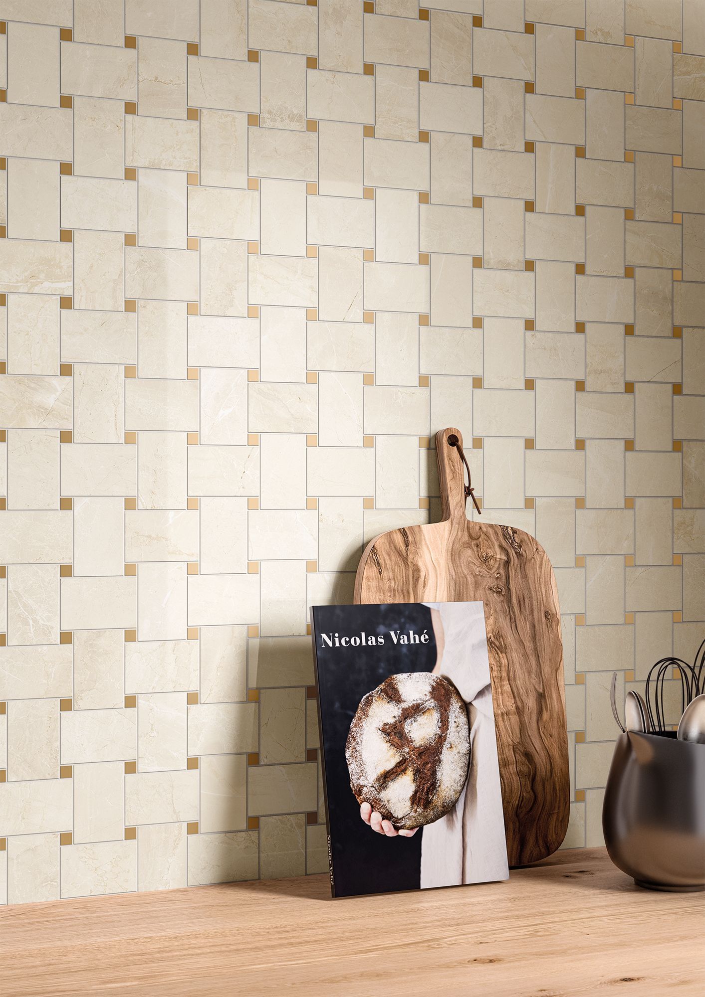 A close-up of a beige marble-effect tile backsplash arranged in a grid pattern. Small square accents in gold enhance the elegance of the design. A wooden cutting board and a cookbook rest on the countertop below.